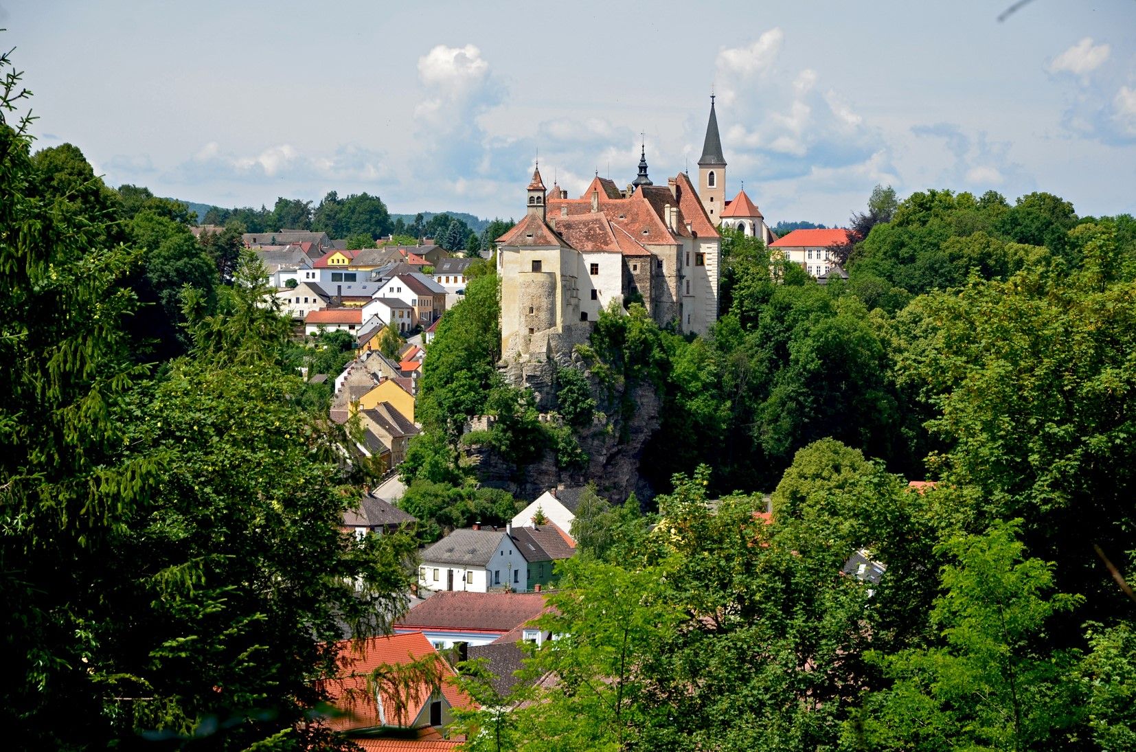 View of the town of Raabs with a castle on a hill, surrounded by trees and houses.
