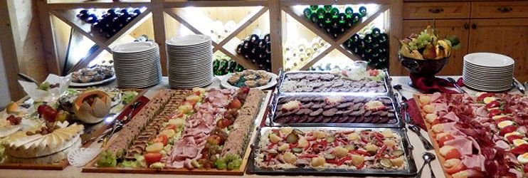 Buffet with various meat and cheese platters in front of a wine rack.
