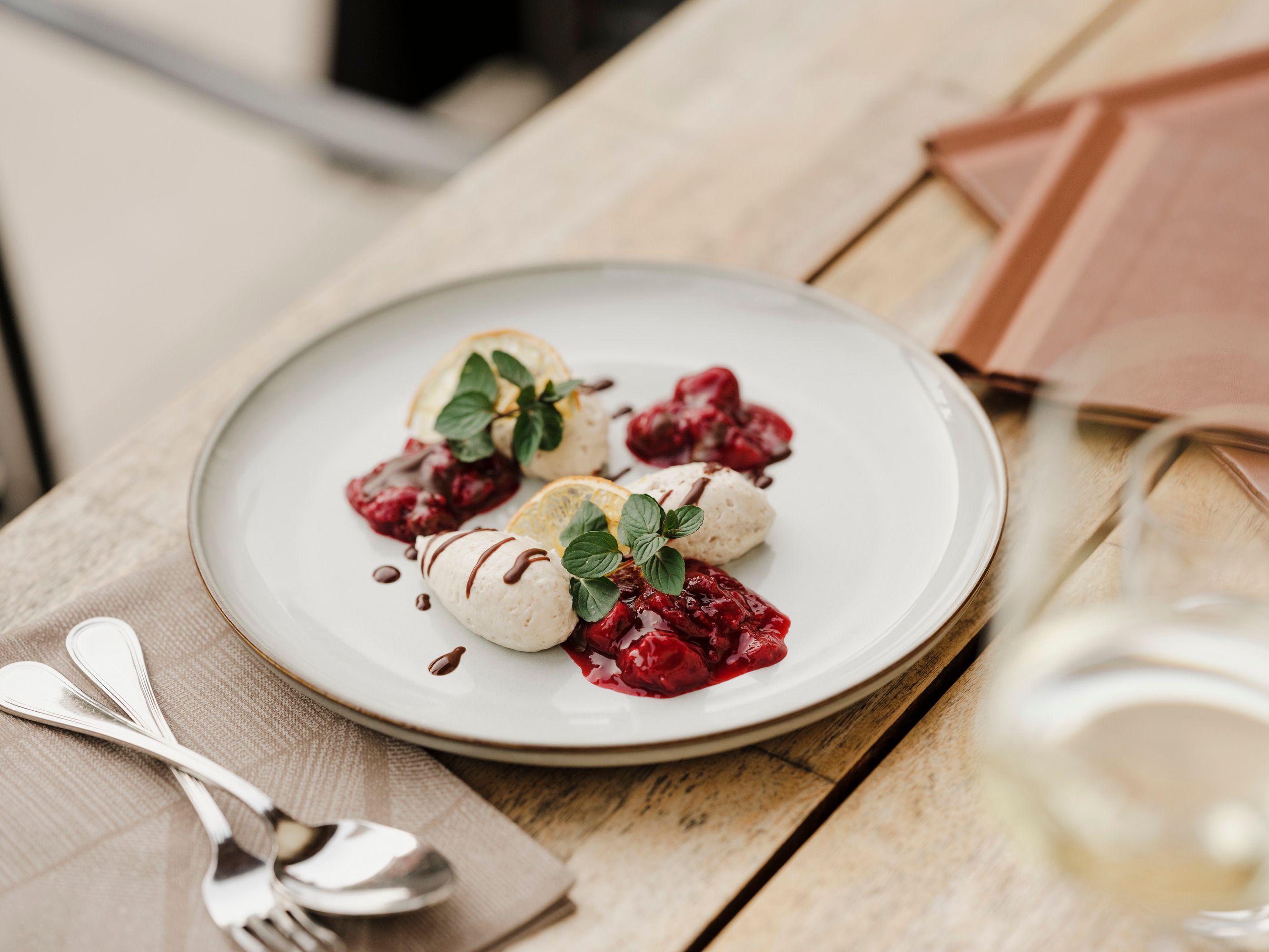 A plate of poppy seed mousse, garnished with berry compote and mint leaves, on a wooden table.