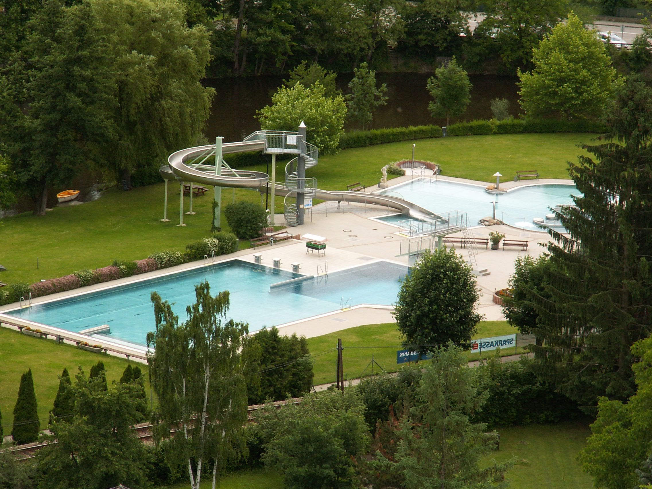 Aerial view of an outdoor pool with slide and pool, surrounded by trees.