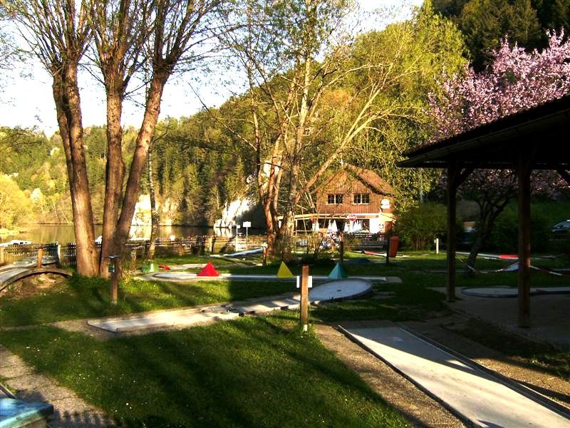 Miniature golf course with trees and a building in the background.