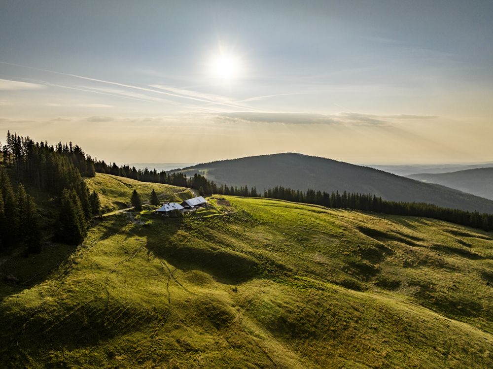 Landscape with green hills, forest and a building under the sun.