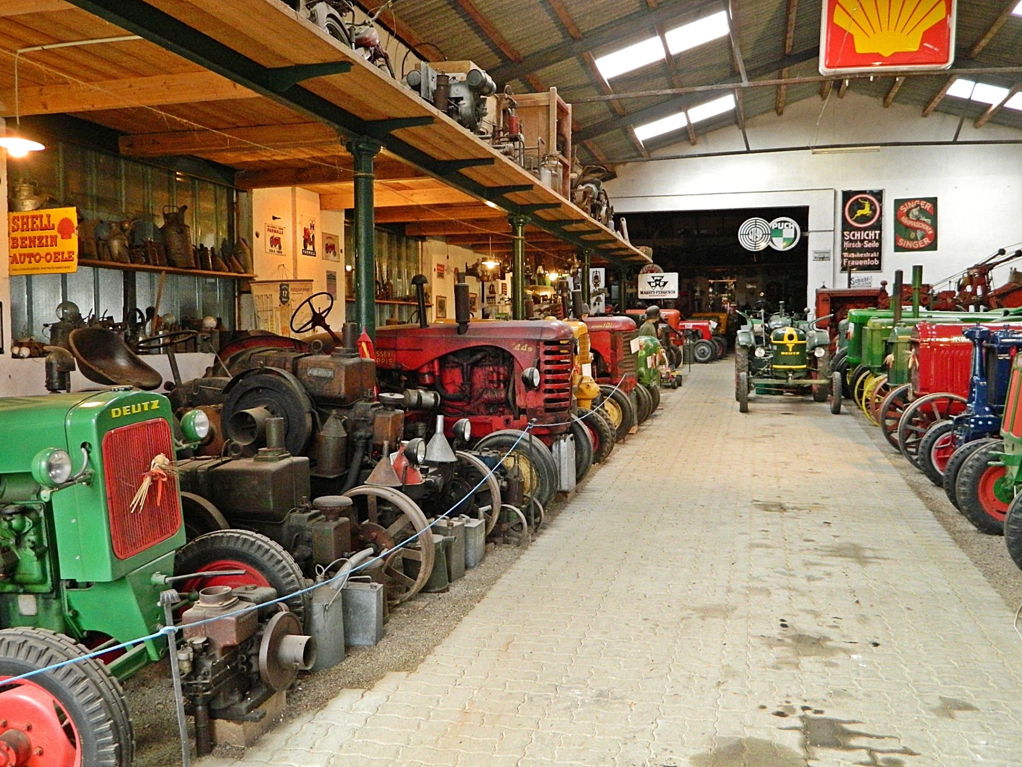 Interior view of a tractor museum with old tractors and advertising signs.