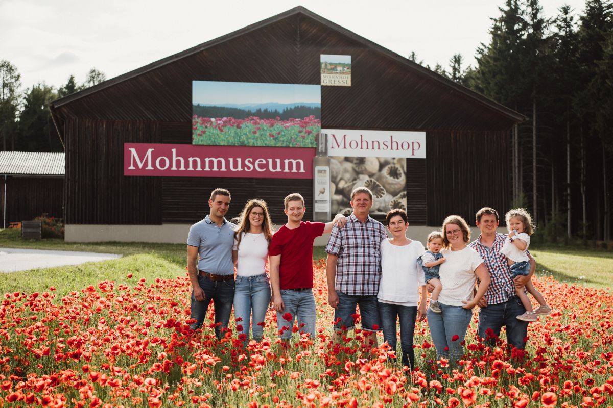 A family stands in a poppy field in front of a building labeled 'Poppy Museum'.