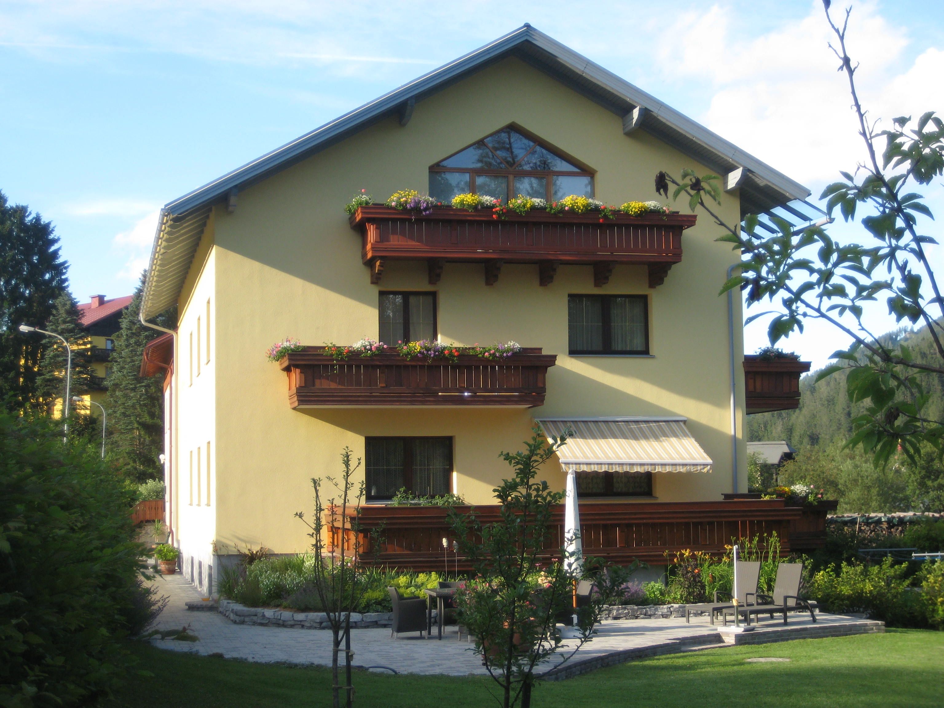 Yellow house with wooden balconies and garden.