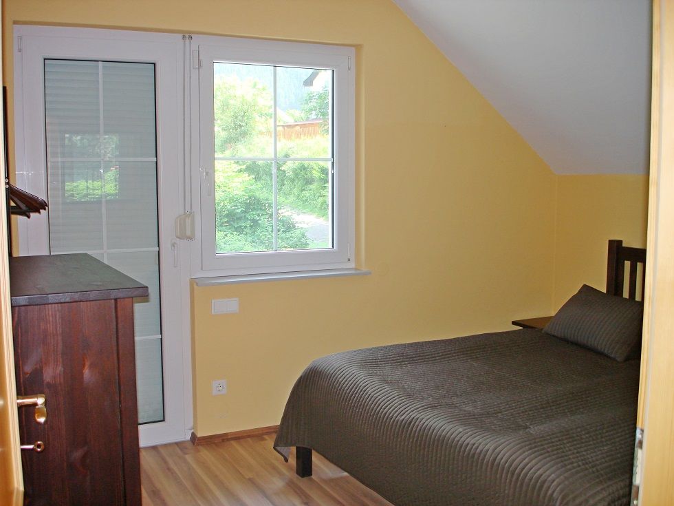A small bedroom with yellow walls, a single bed and a window with a view of the greenery.