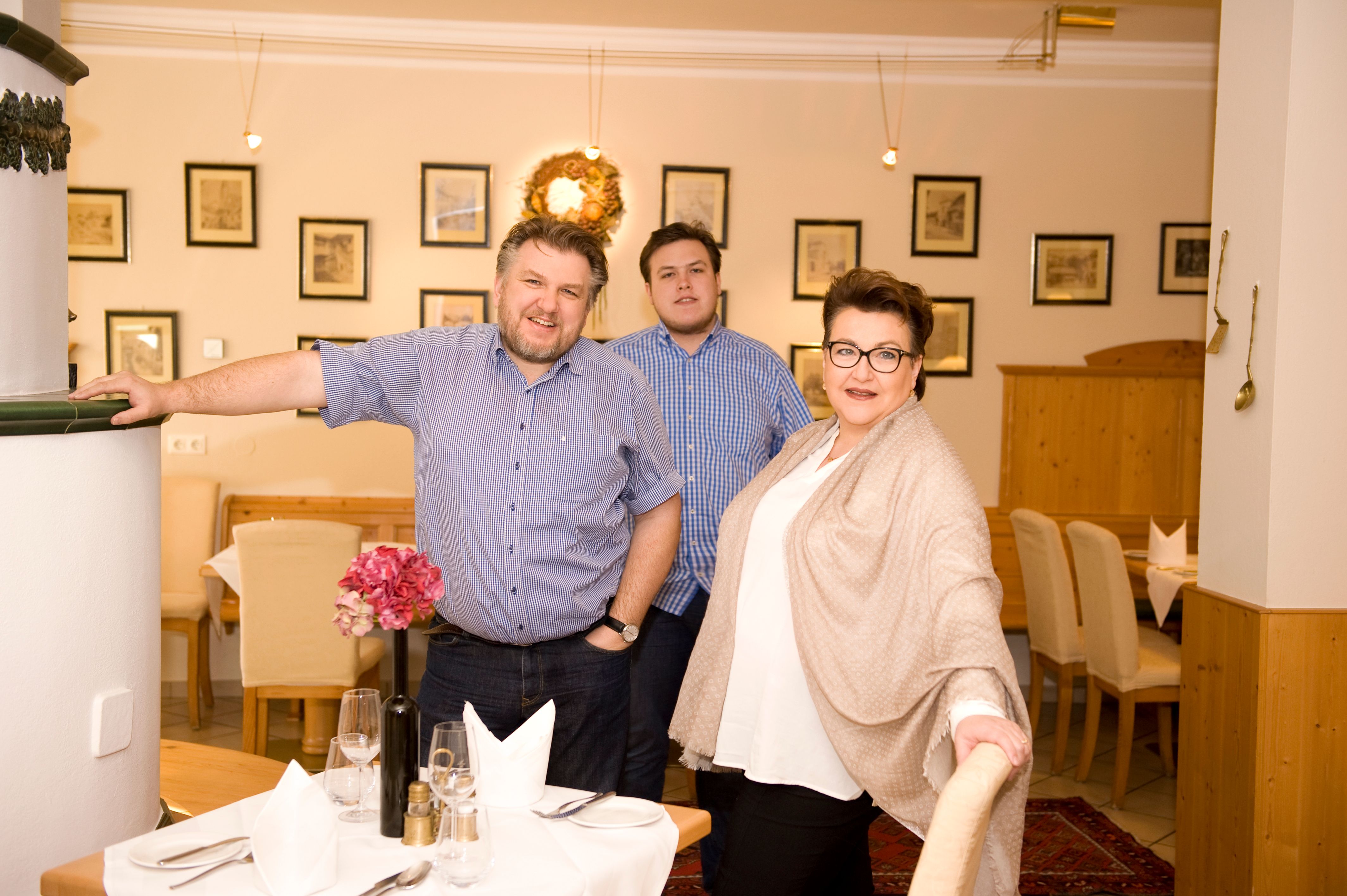 The host family in a restaurant, smiling and looking at the camera. The room is decorated with pictures and a wreath.