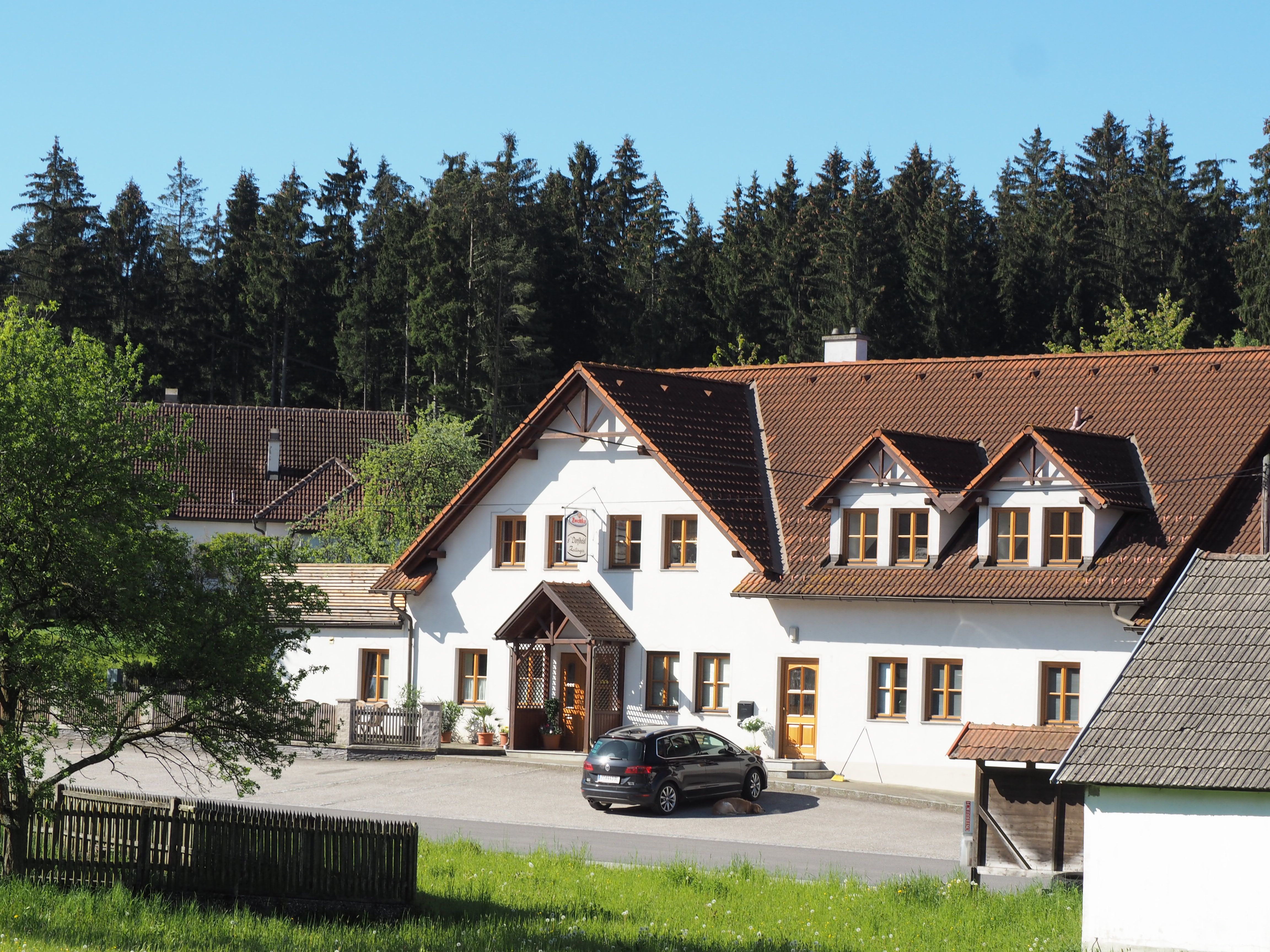 A traditional inn with a white façade and brown roof, surrounded by trees and meadows.