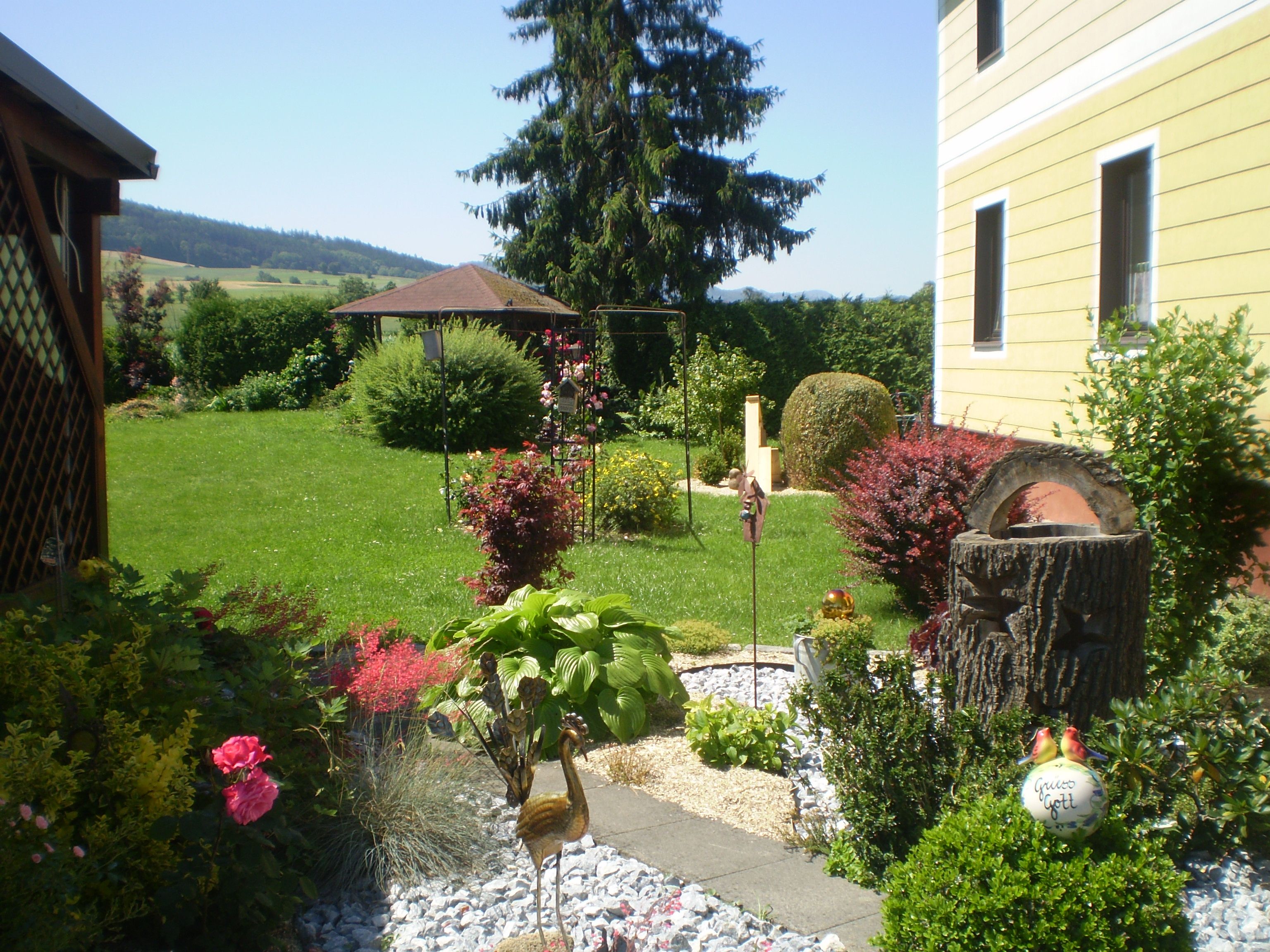 A well-tended garden with flowers, shrubs and a yellow house in the background.