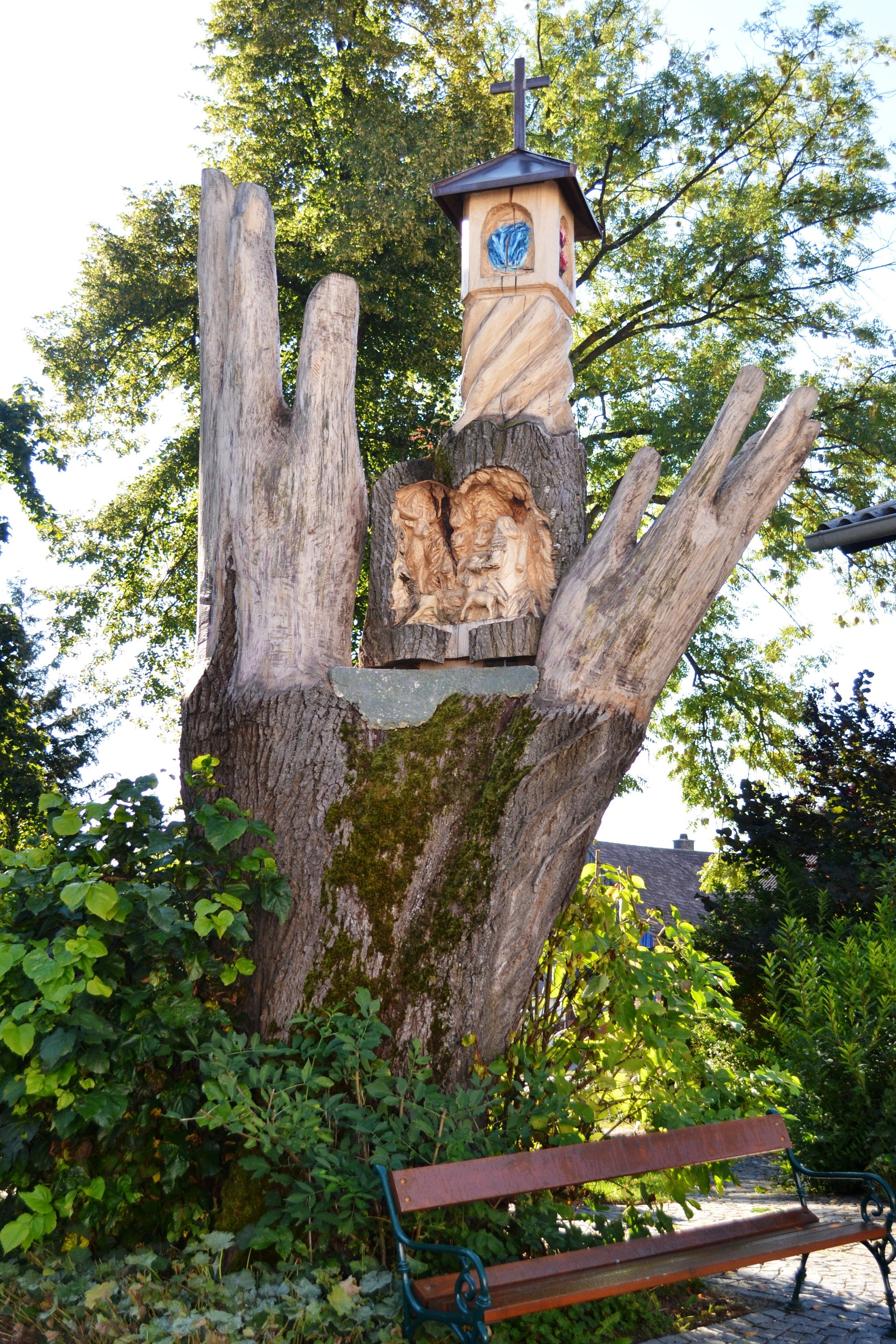 Wooden sculpture in the shape of a hand with carved figures and a small tower with a cross.