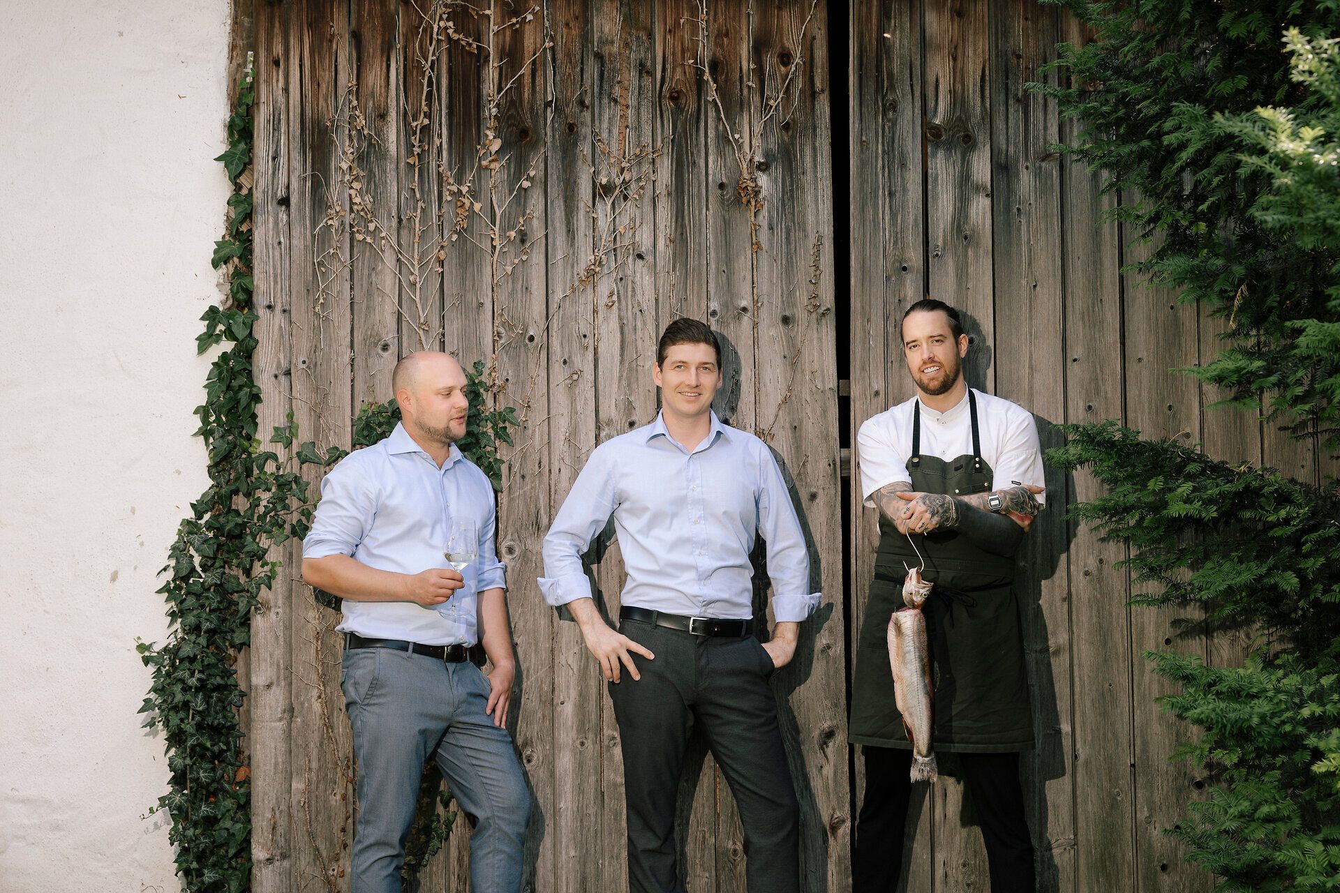 Three men are standing in front of a wooden wall