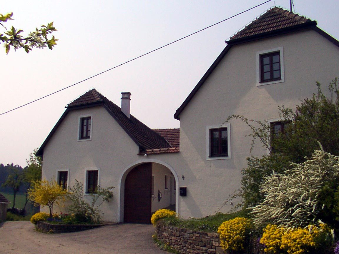 A white country house with a brown roof and garden.