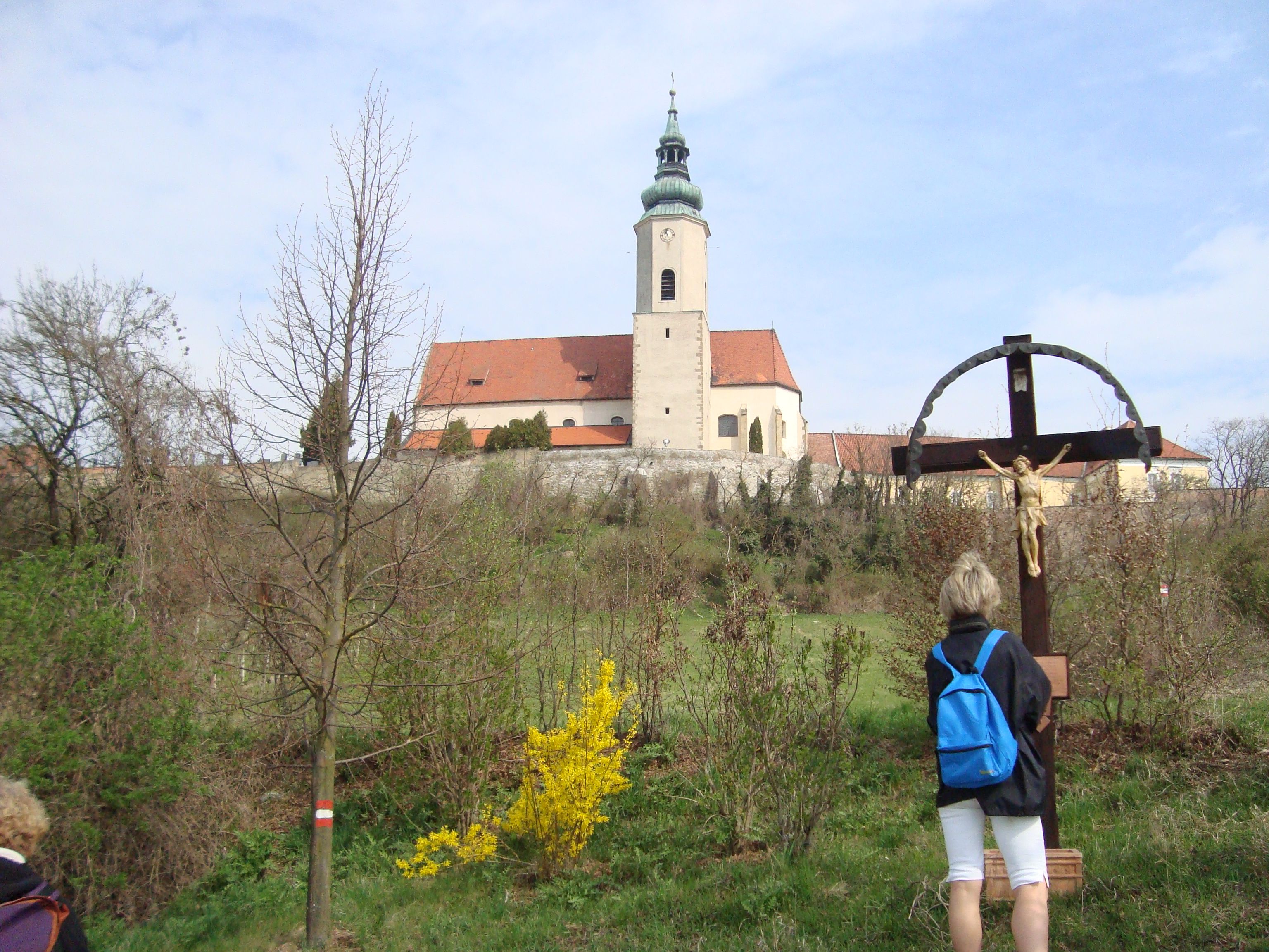 A church on a hill with a cross in the foreground and a person looking at the cross.