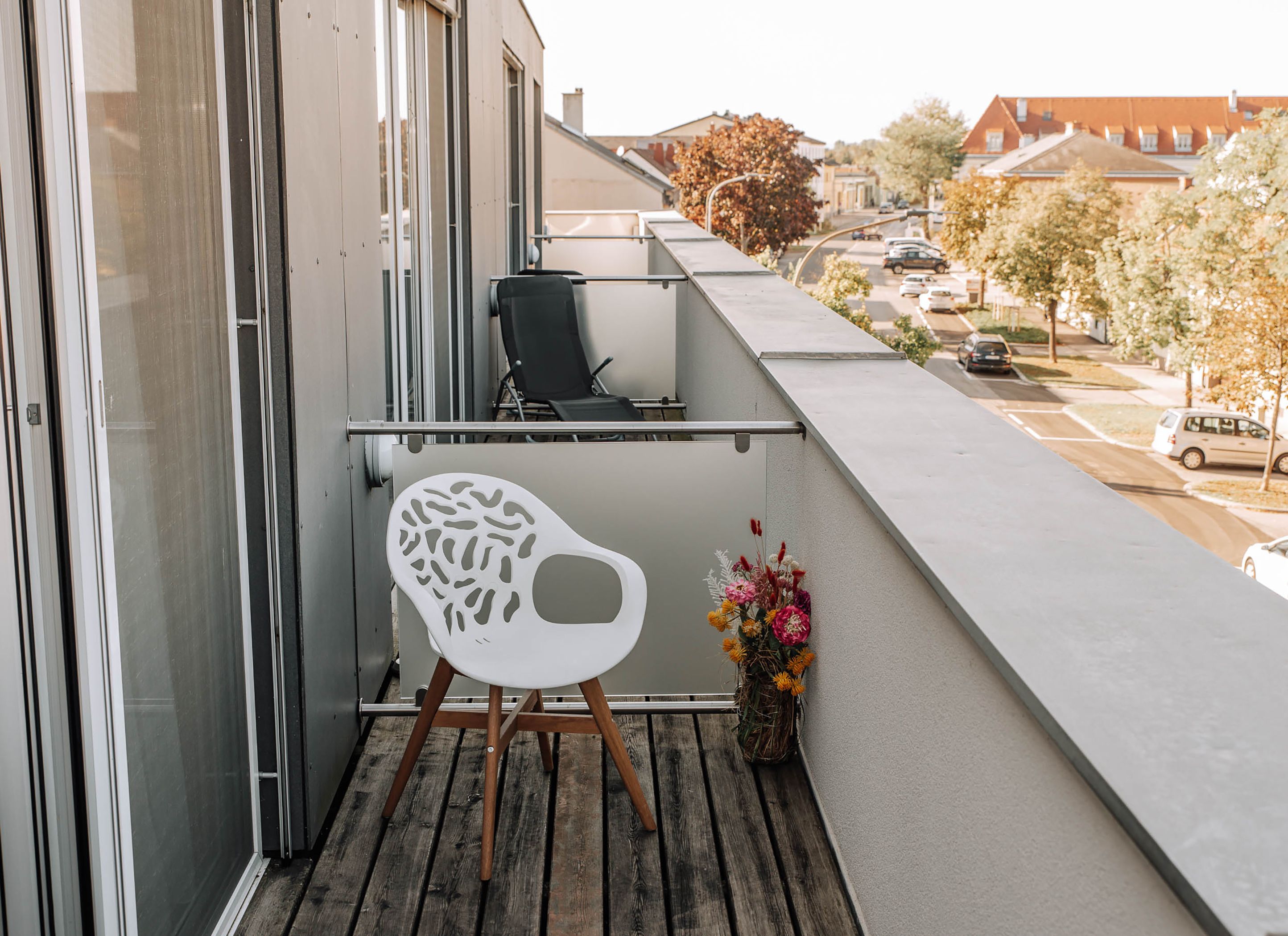 Balcony with white chair and bouquet of flowers, view of the street and building.
