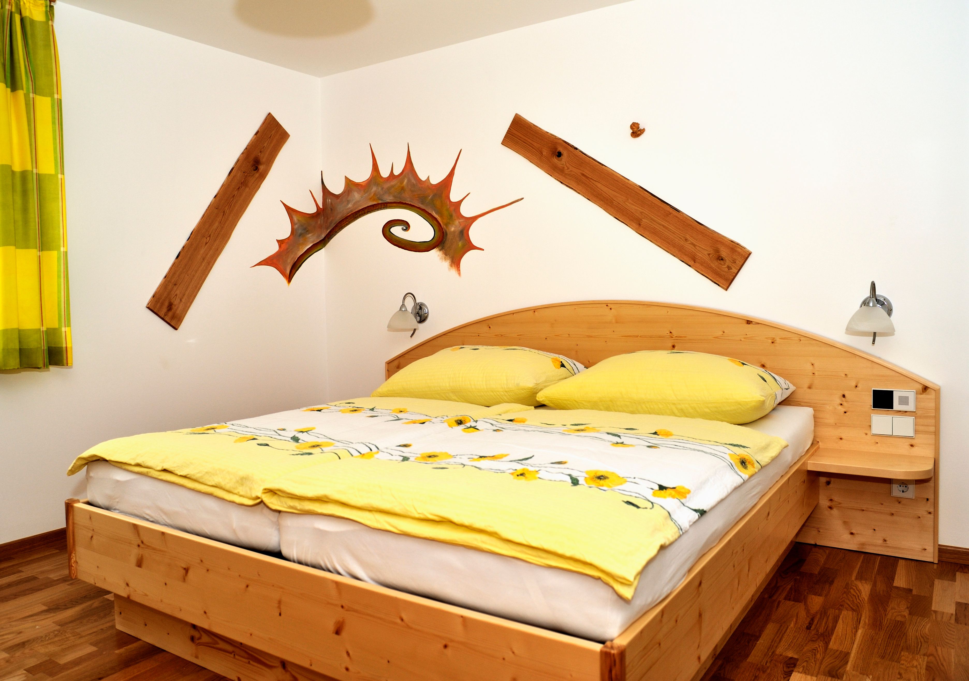 A cozy bedroom with a wooden bed, yellow bed linen and decorative wooden elements on the wall.