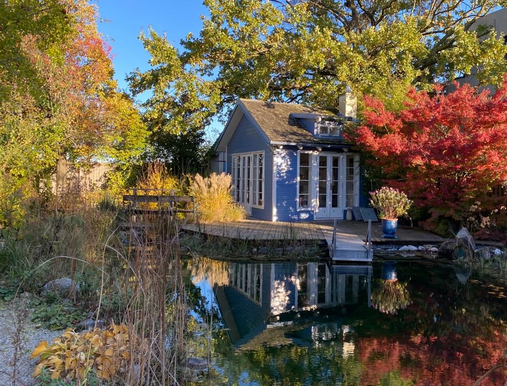 Small blue house by the pond, surrounded by colorful autumn trees.