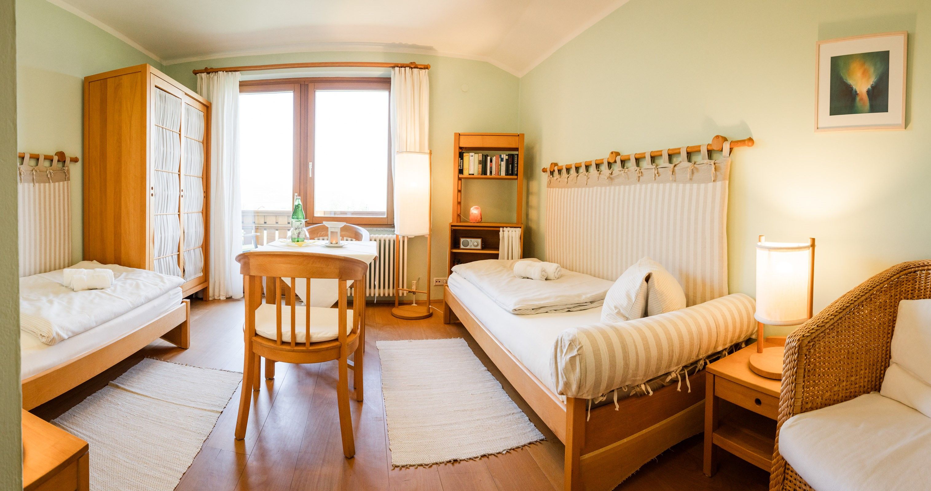 Comfortable twin room with wooden furniture, two beds, table, chairs and a window with curtains.