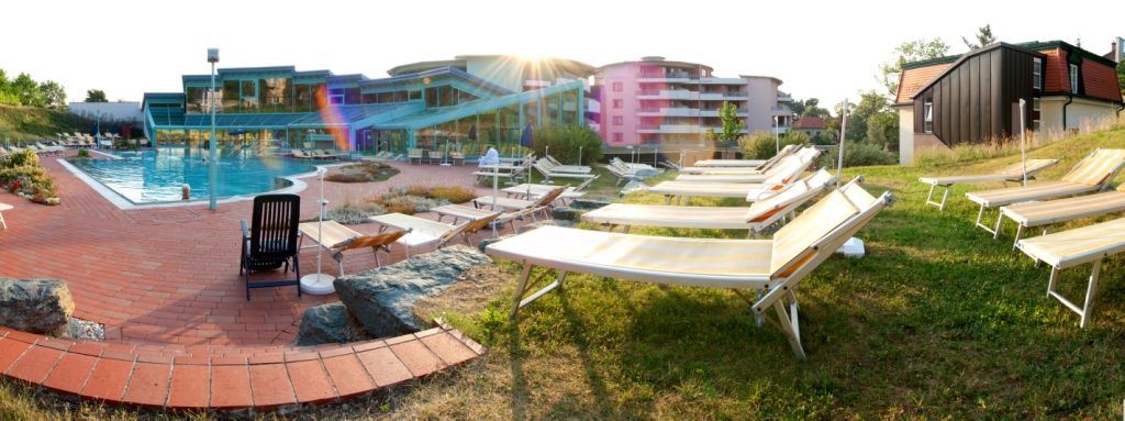 A pool area with sun loungers and a modern building in the background.
