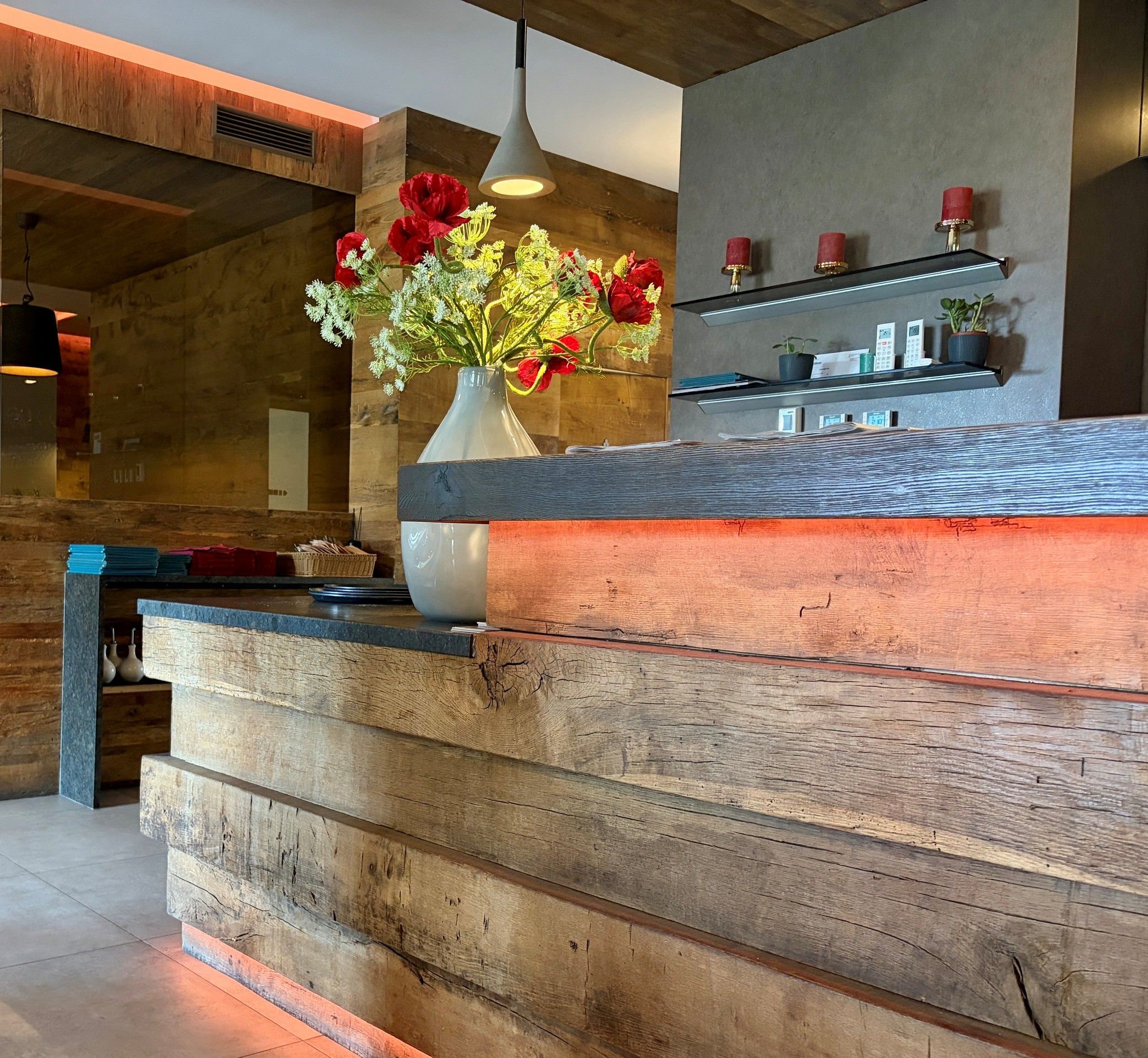 A stylish reception area with wooden accents and a vase of red flowers on the counter.