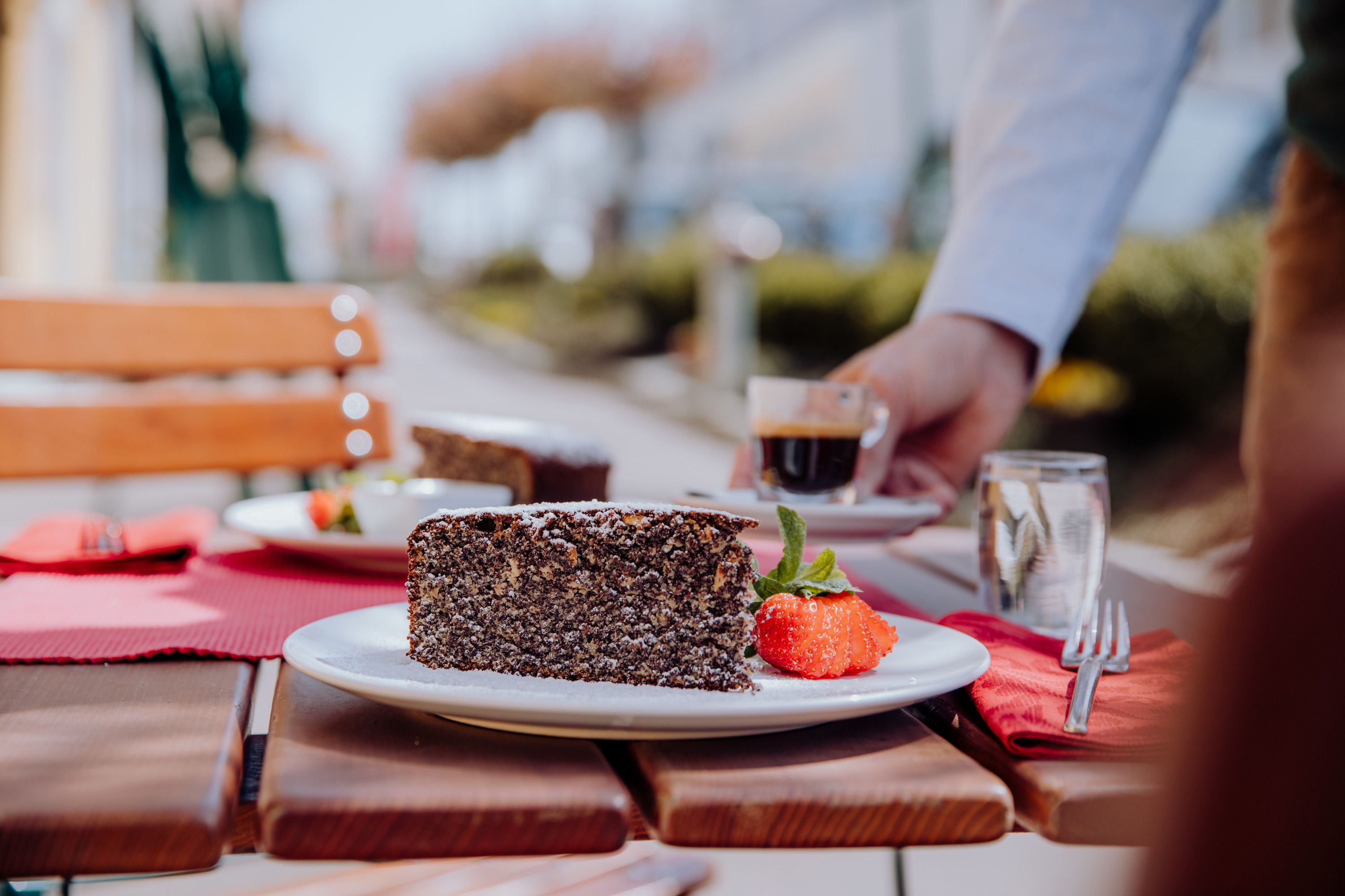 Poppy seed cake with strawberry and espresso served on a wooden table outside.