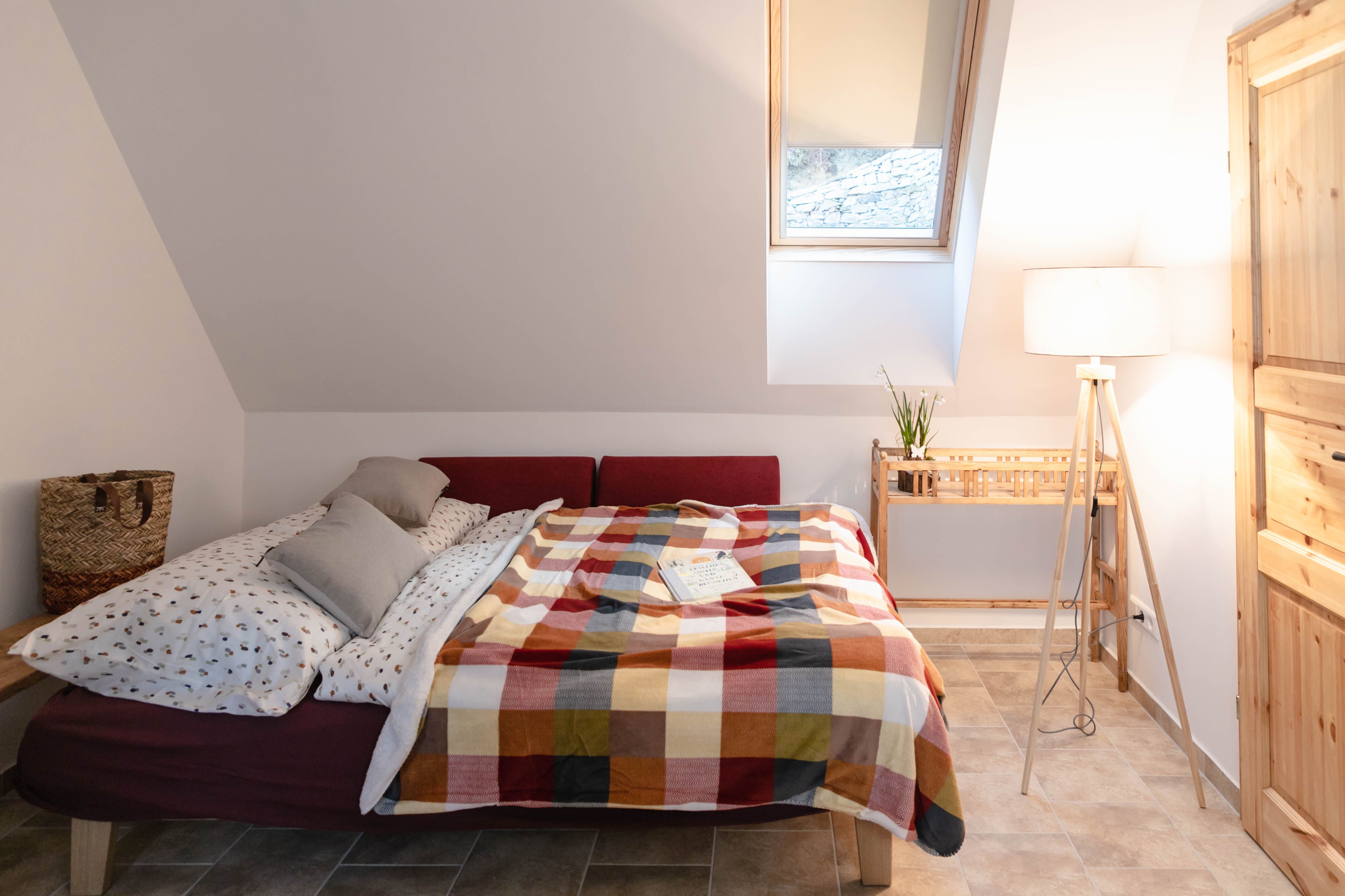 Cozy bedroom with bed, colorful blanket and reading lamp.