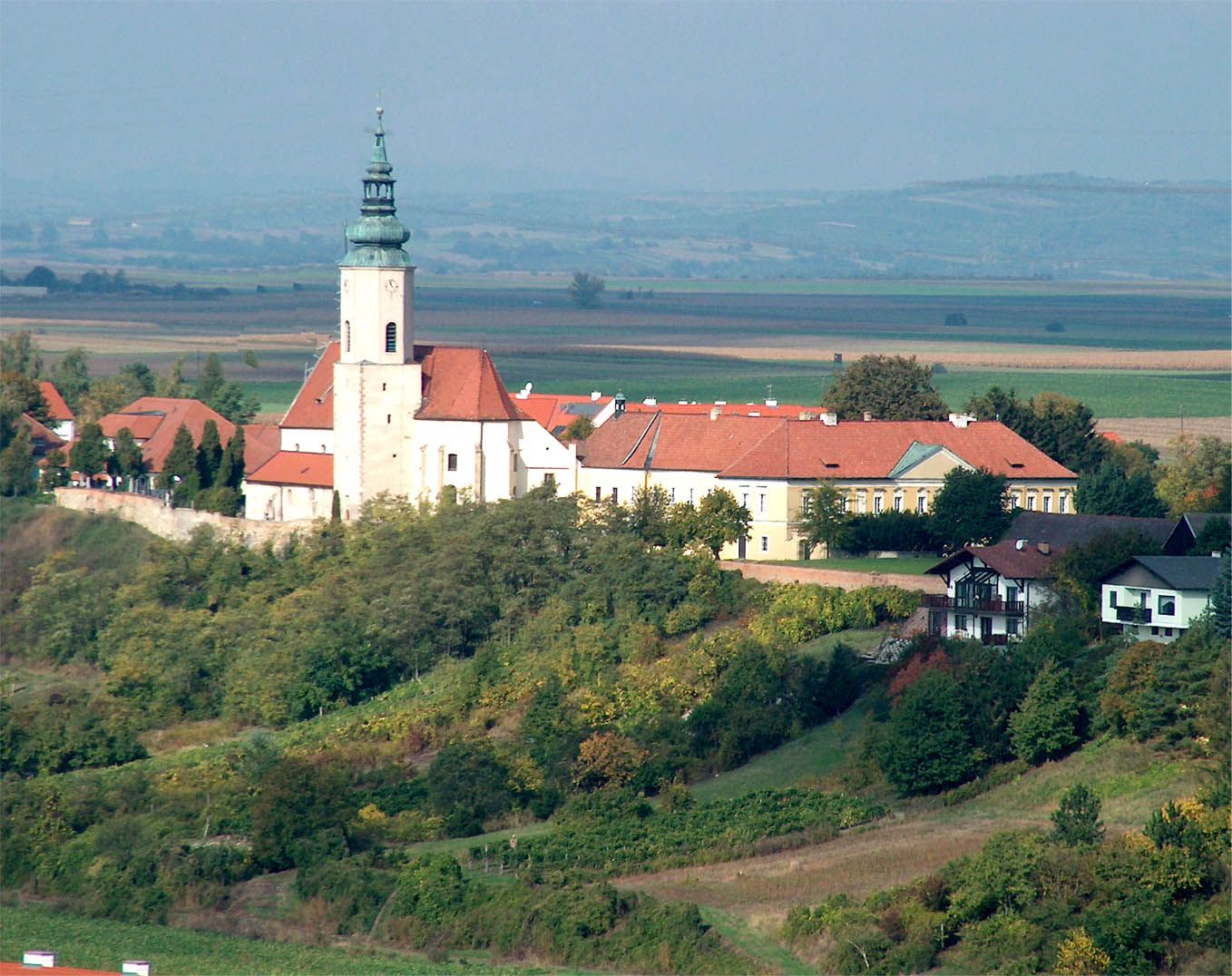 Parish church of St. Agatha on a hill with surrounding buildings and landscape in the background.