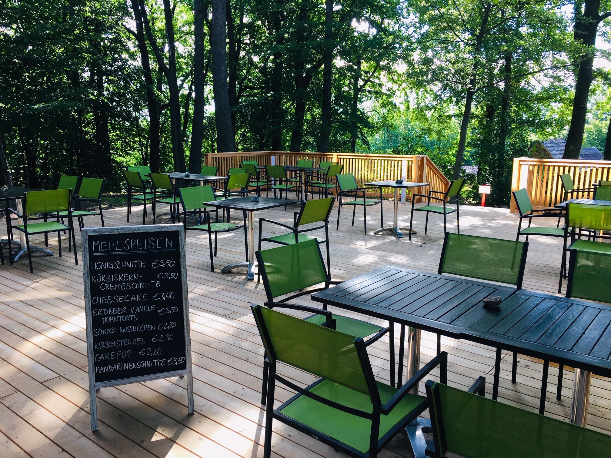Terrace area in the Turmcafé with square tables, green chairs and wooden fence.
