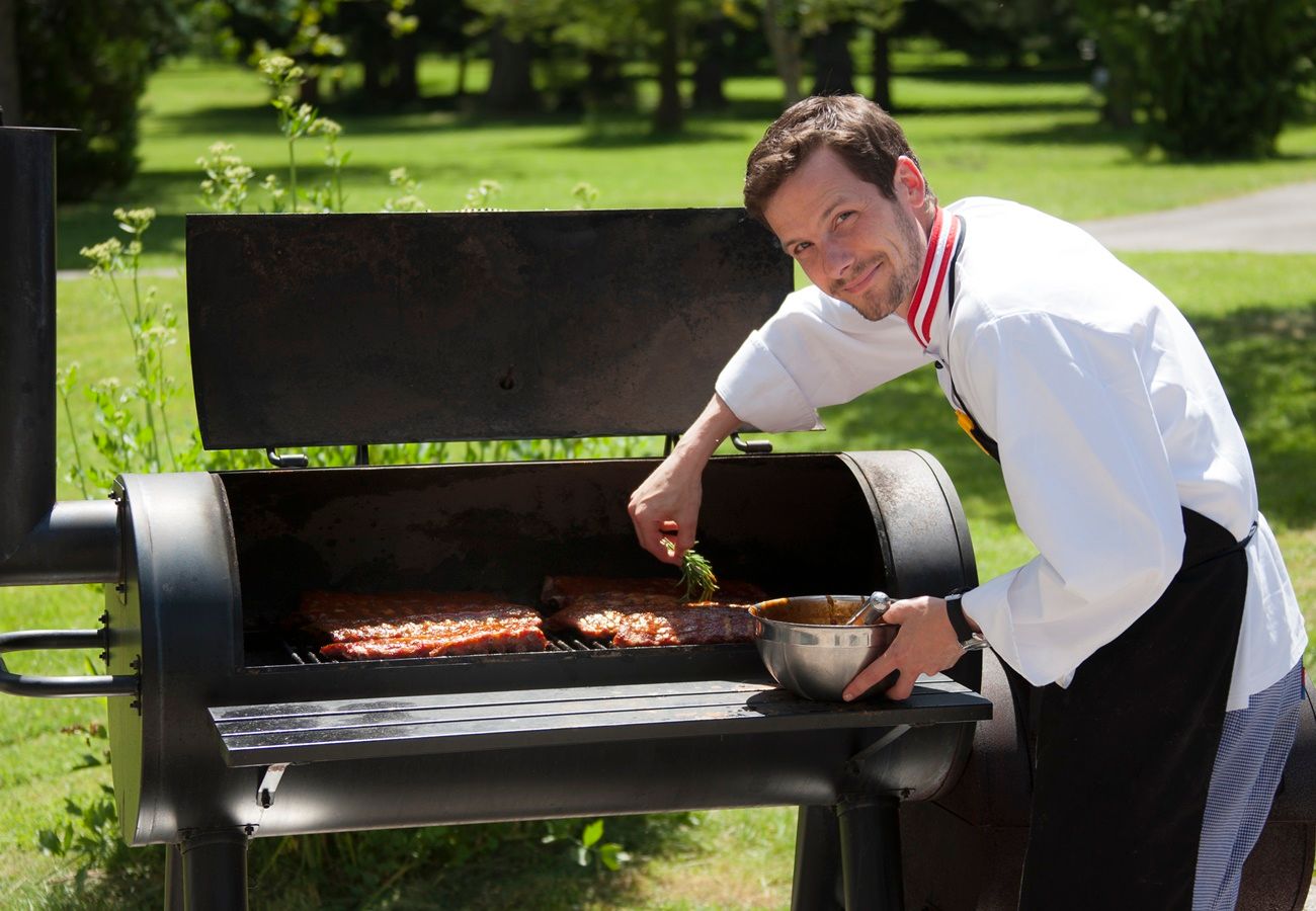 A cook grills meat on a large outdoor grill.