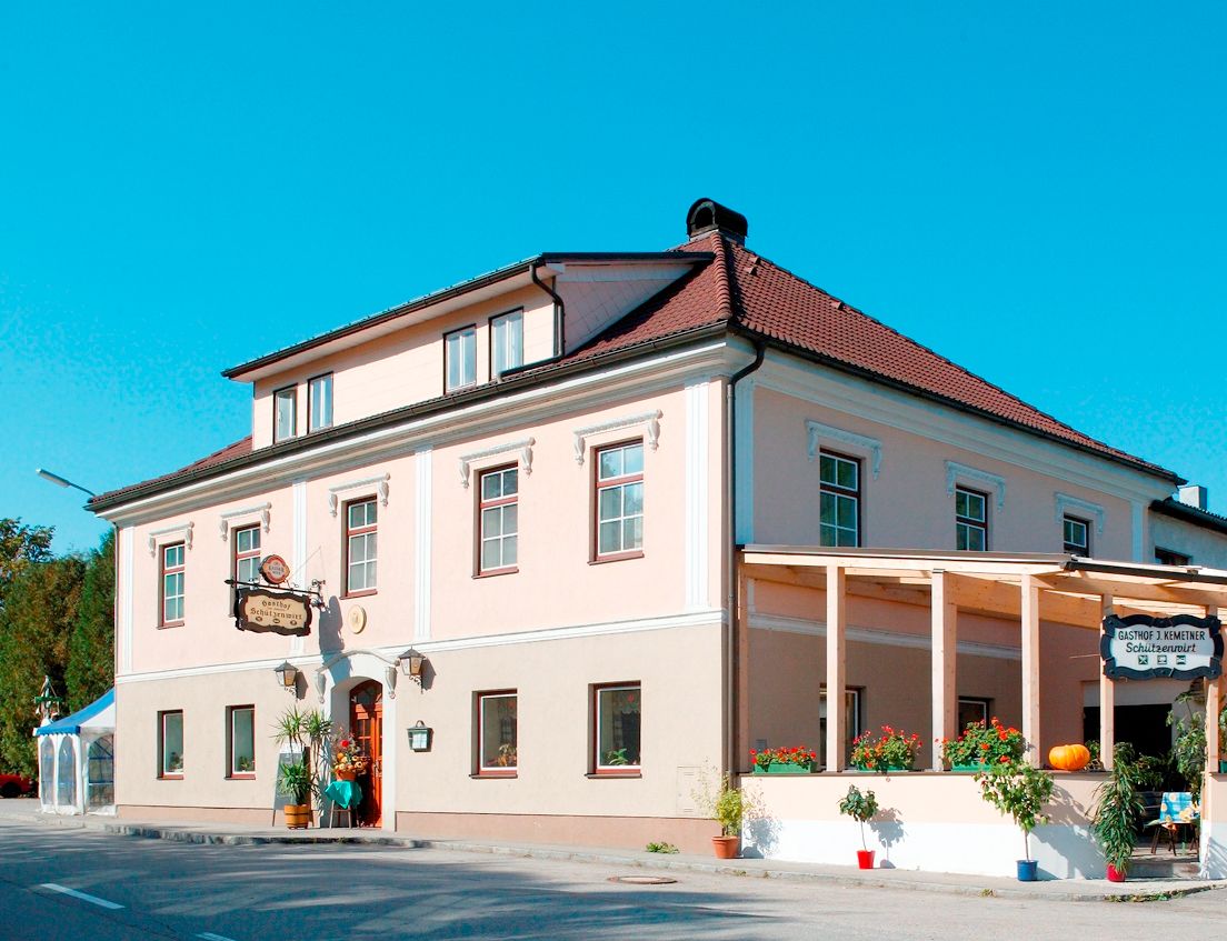 A traditional inn with a pink façade and red roof, decorated with plants and a pumpkin.