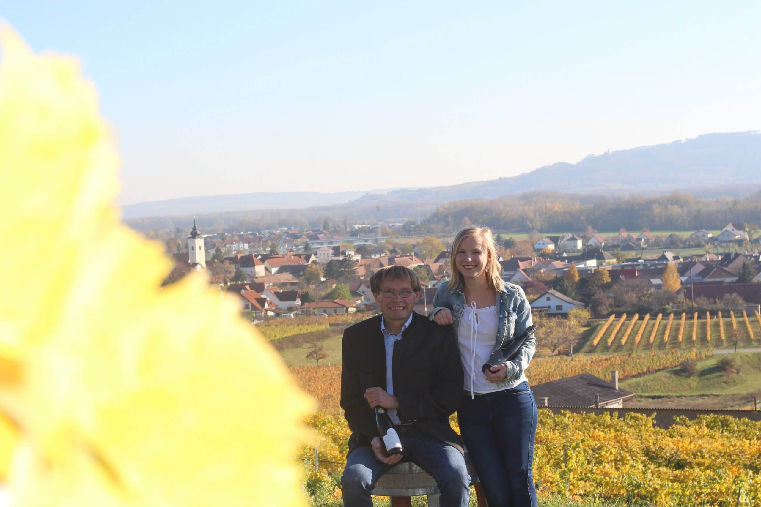 Two people in a vineyard with a view of a village in the background.