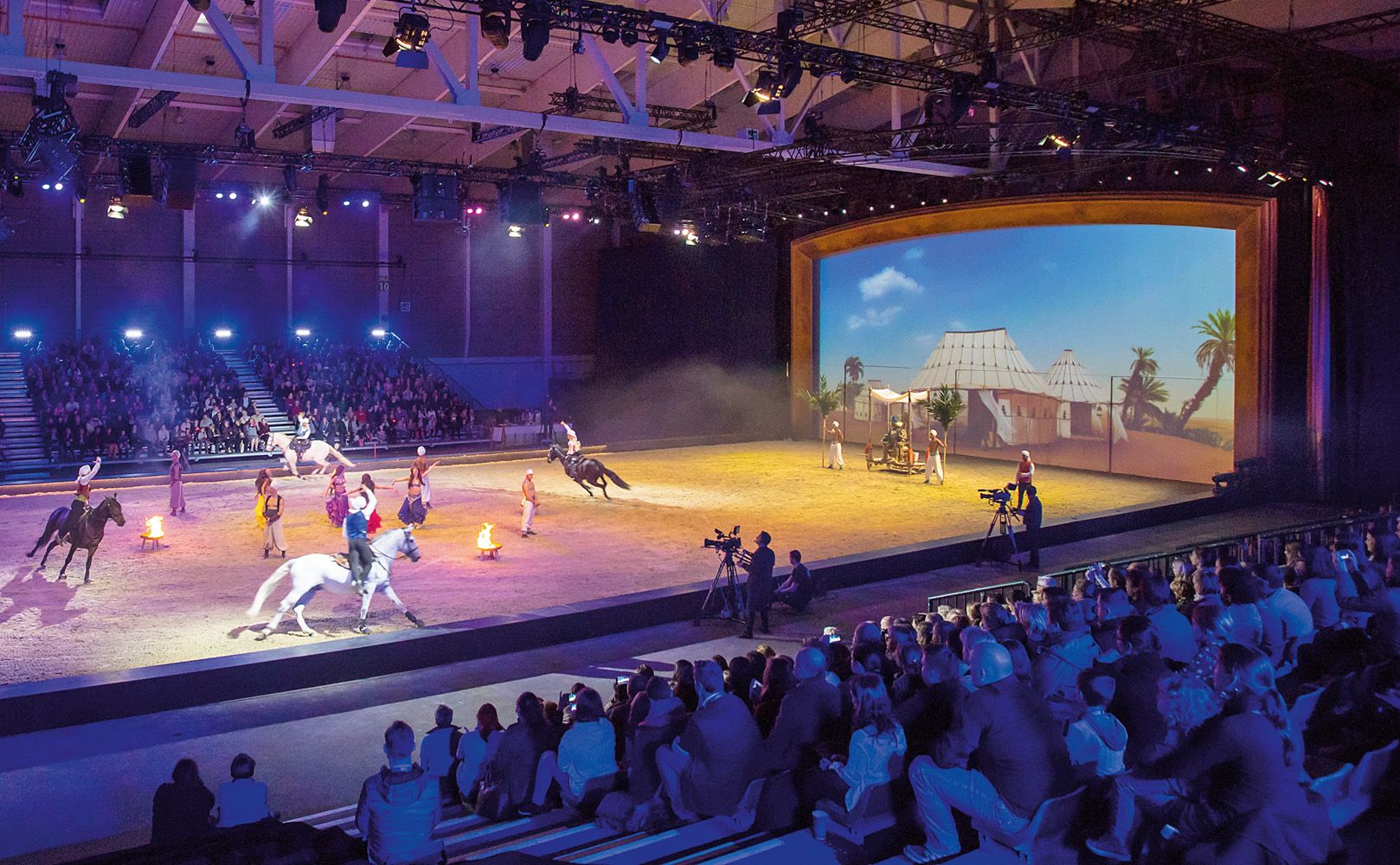 Horse show in a large hall with audience and stage design.