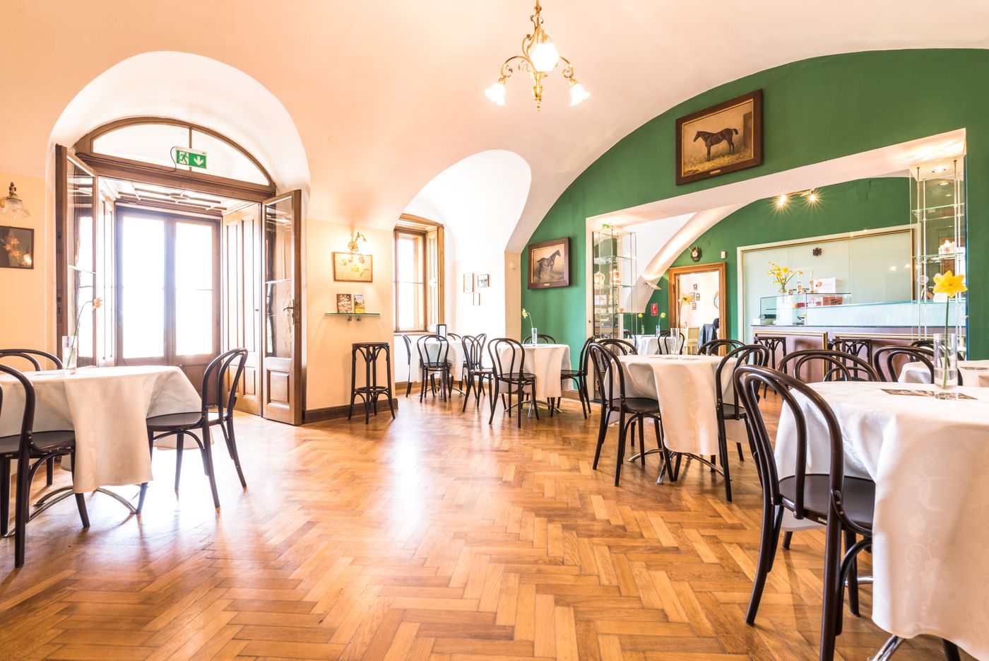 Interior view of an elegant café with wooden floor, white tablecloths and green wall.
