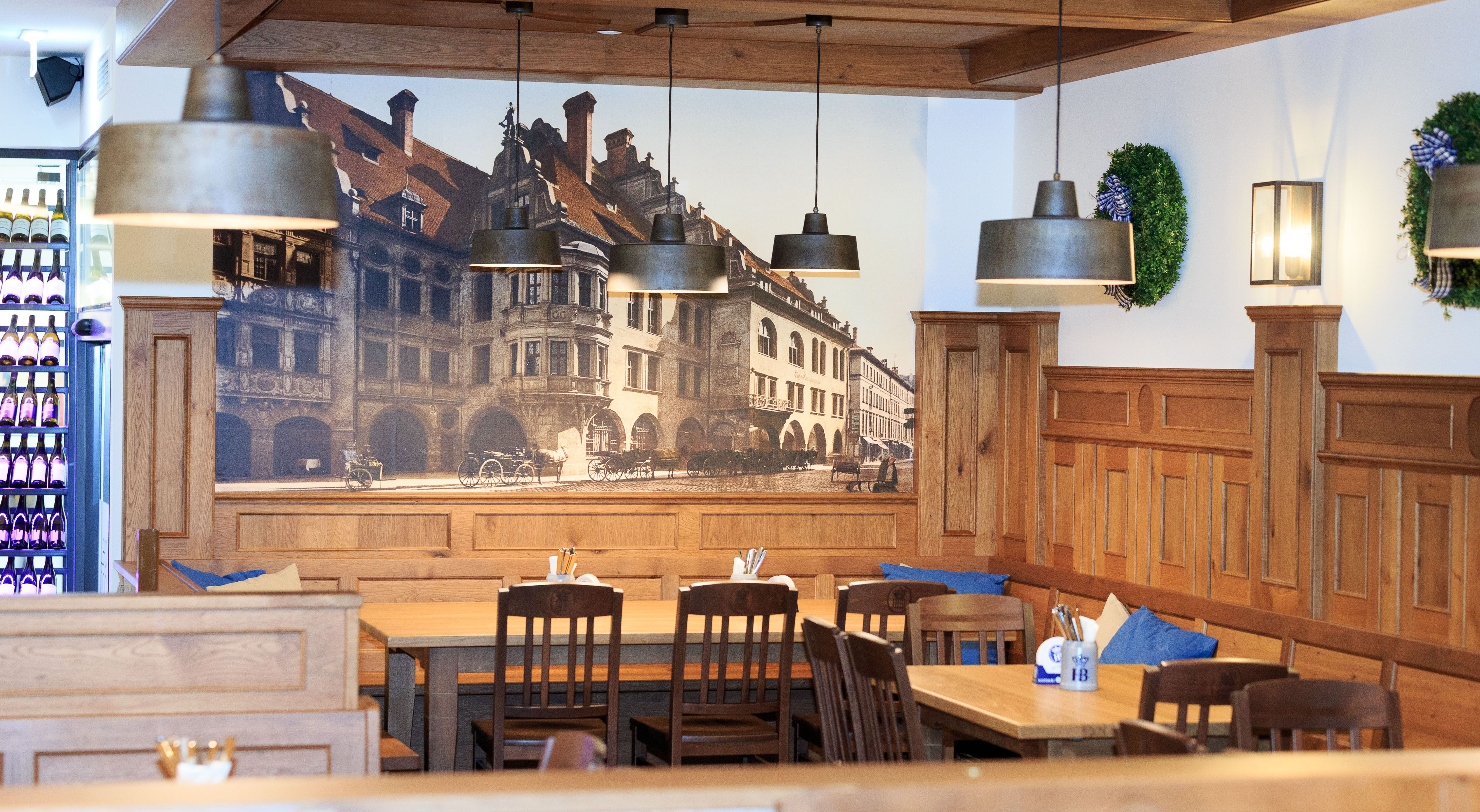 Interior view of a traditional Bavarian restaurant with wooden furniture and mural of the Hofbräuhaus.