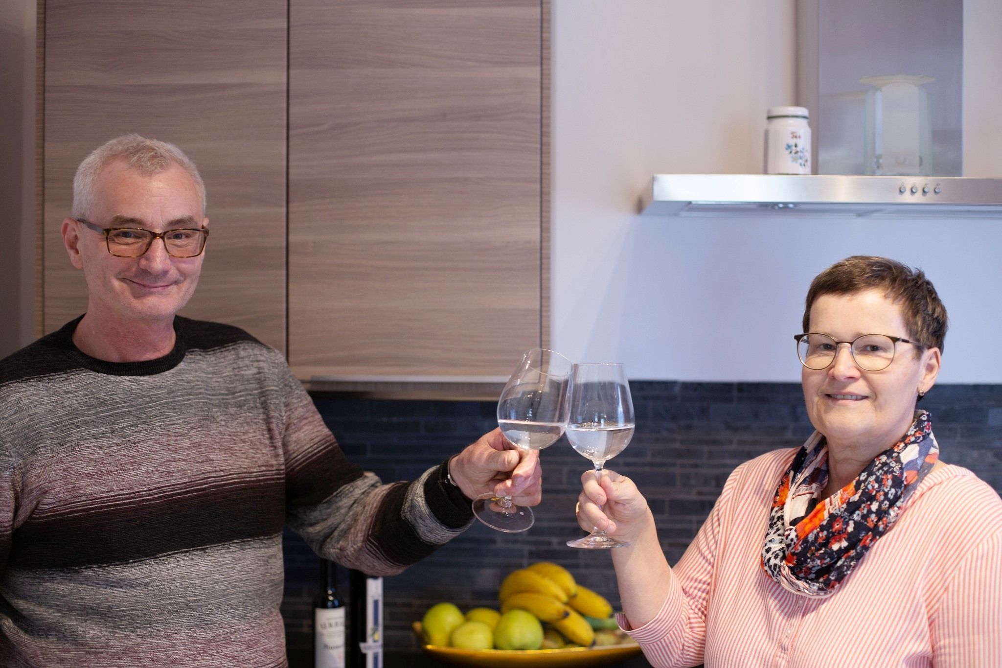 Two people clink glasses of wine in a kitchen.