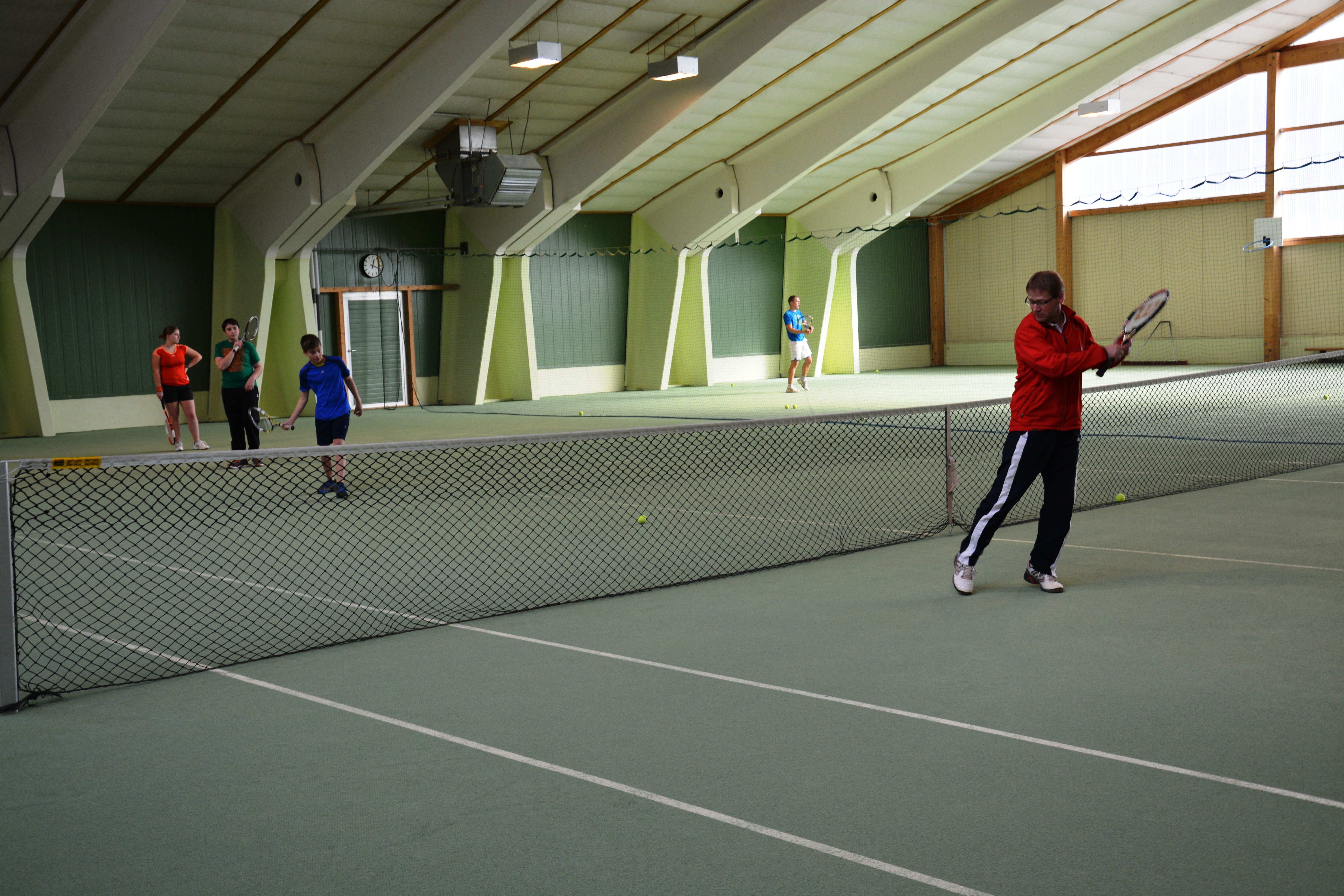 People play tennis in an indoor tennis hall.