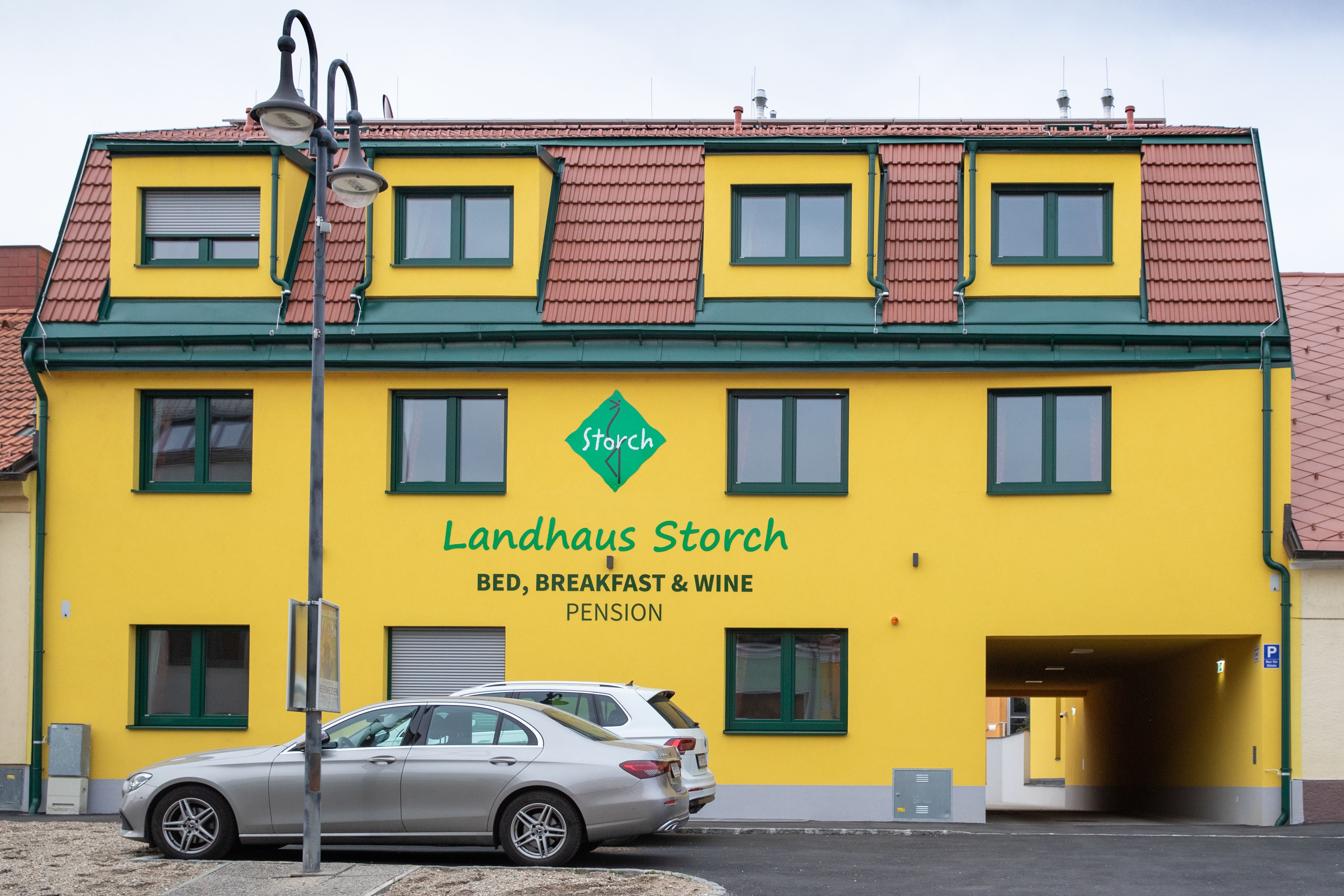 Yellow building with the inscription 'Landhaus Storch', cars parked in front of it.