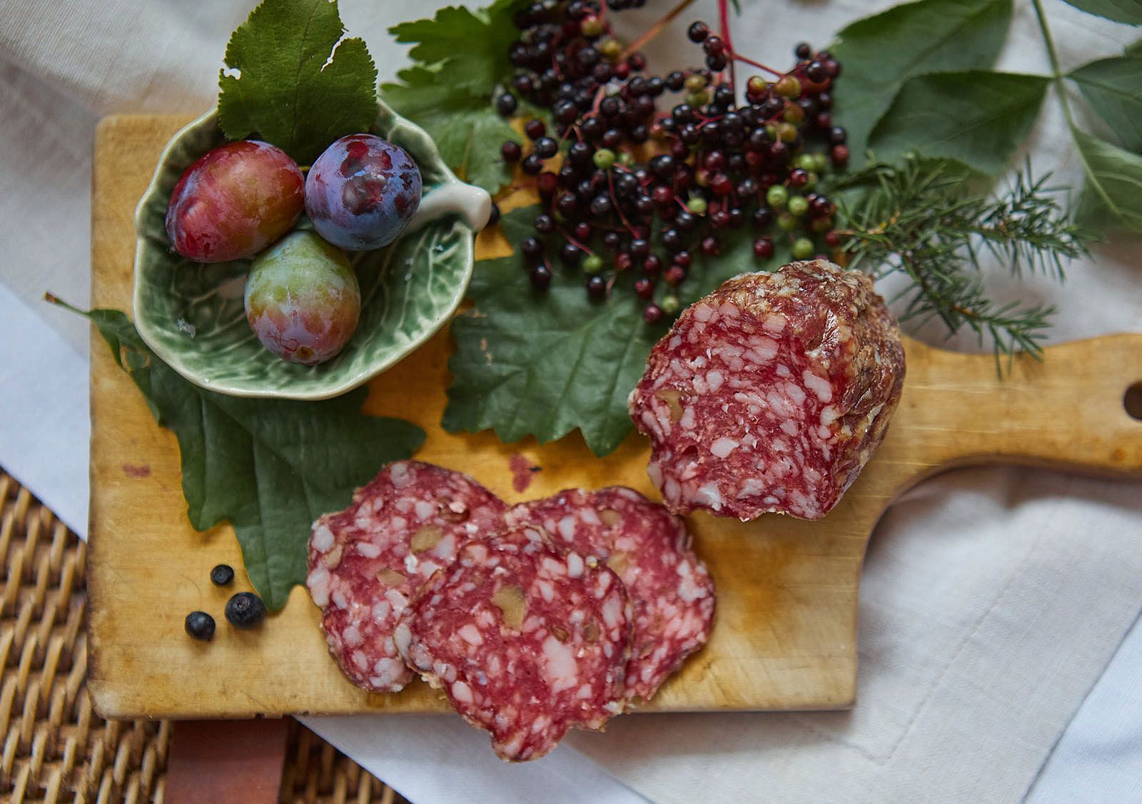 Close-up of a salami on a wooden board with berries and plums.