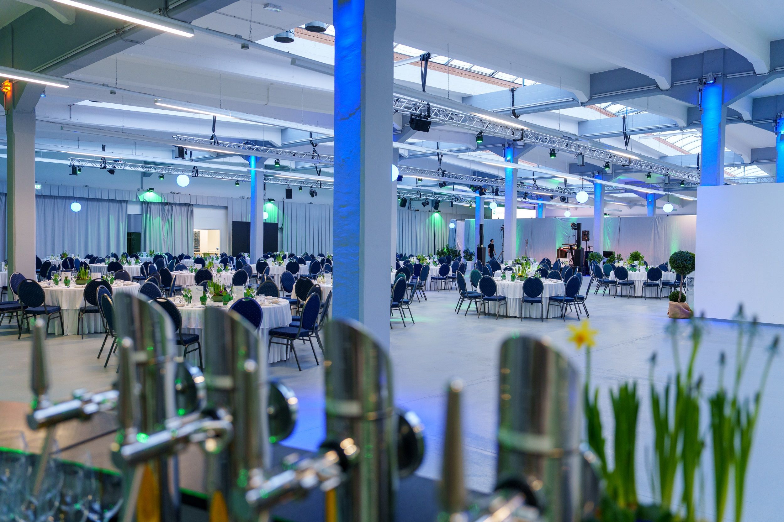 Large function room with round, laid tables and blue lighting.