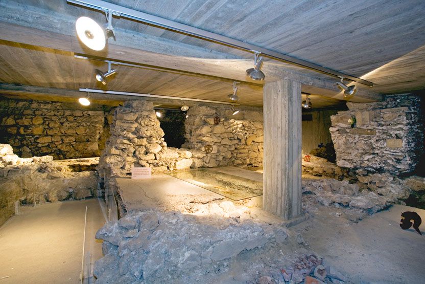 Underground ruins with stone walls and concrete pillars, illuminated by ceiling spotlights.