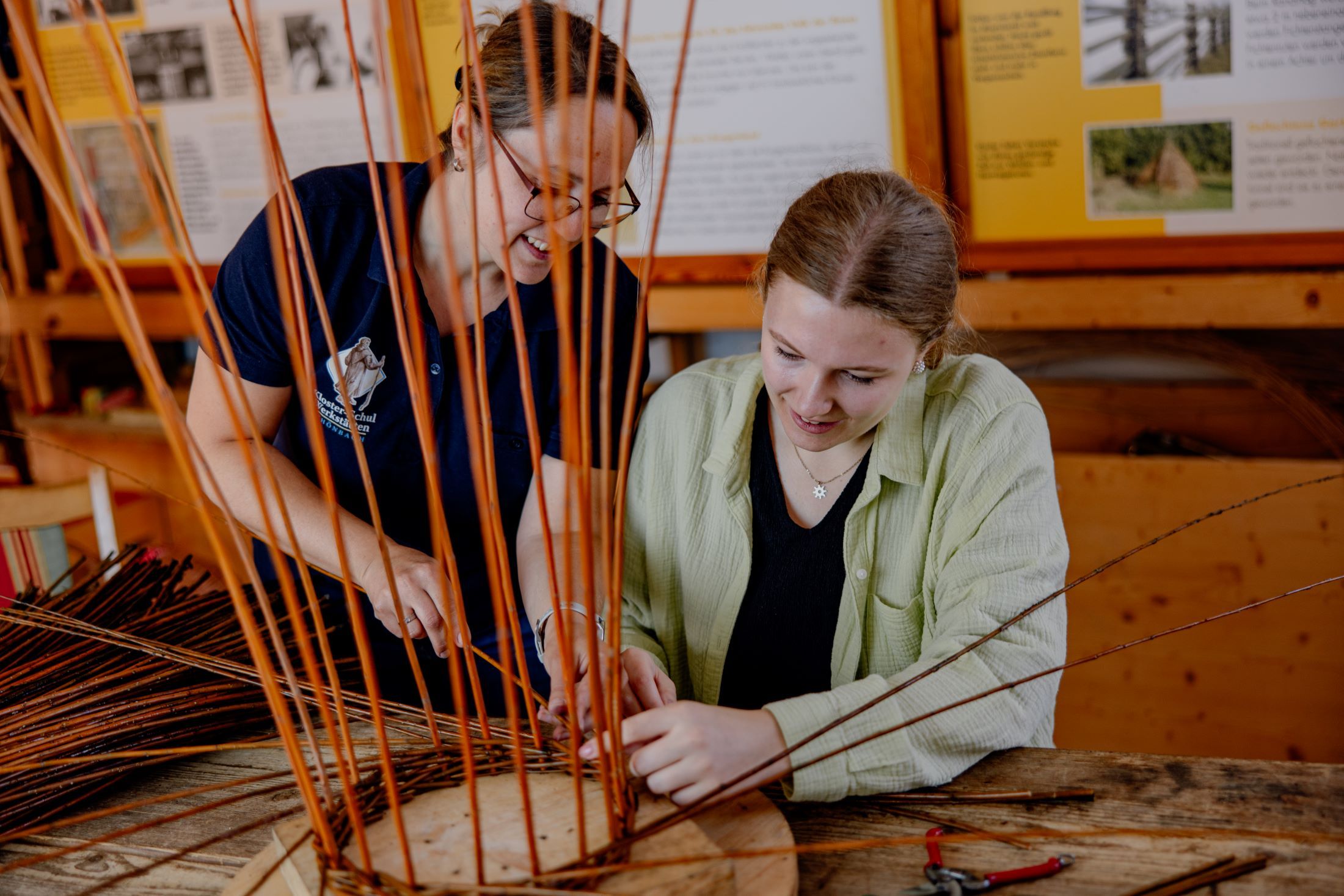 Two women work together on a basket weaving project in a workshop.