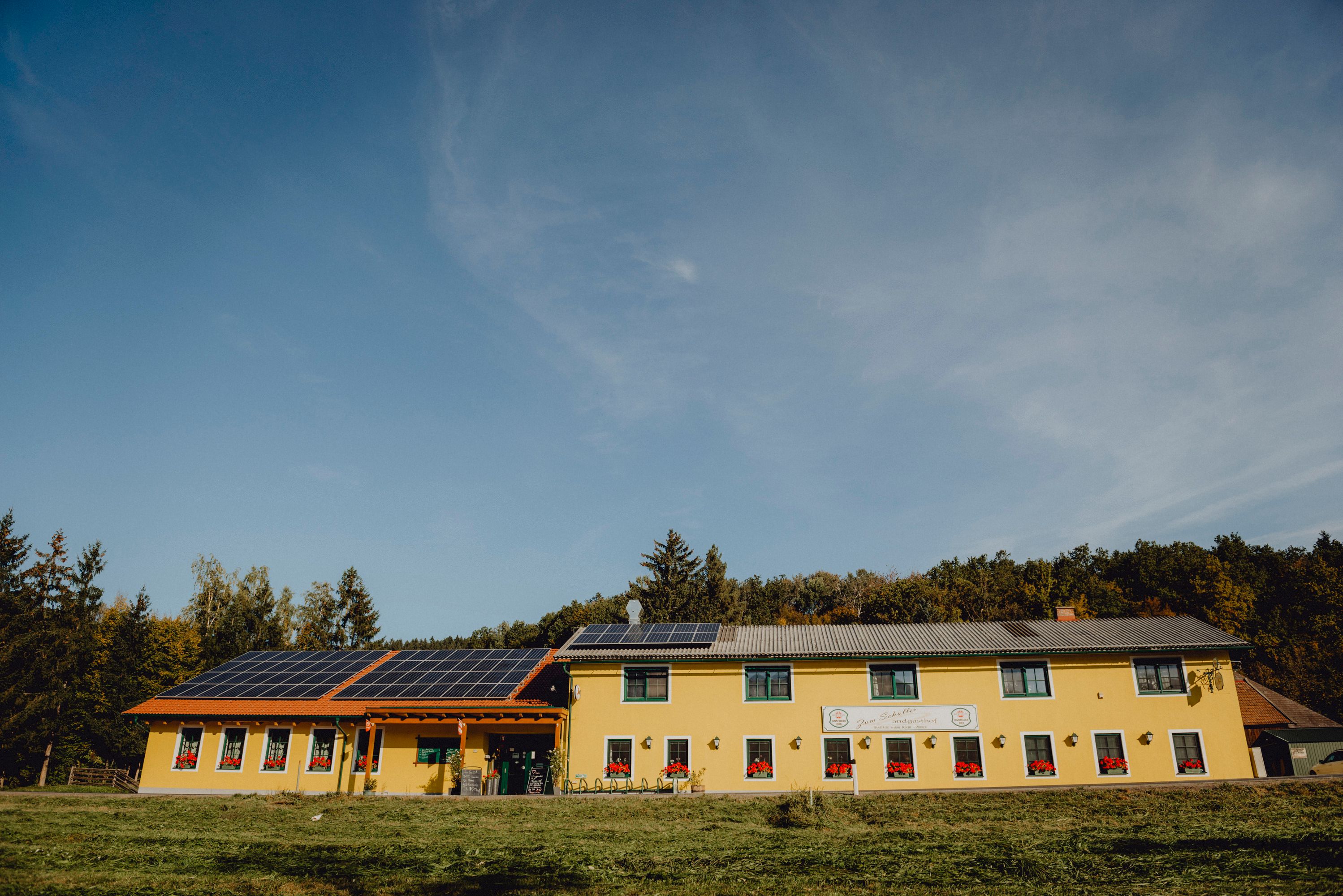 Yellow building with solar panels on the roof, surrounded by trees.