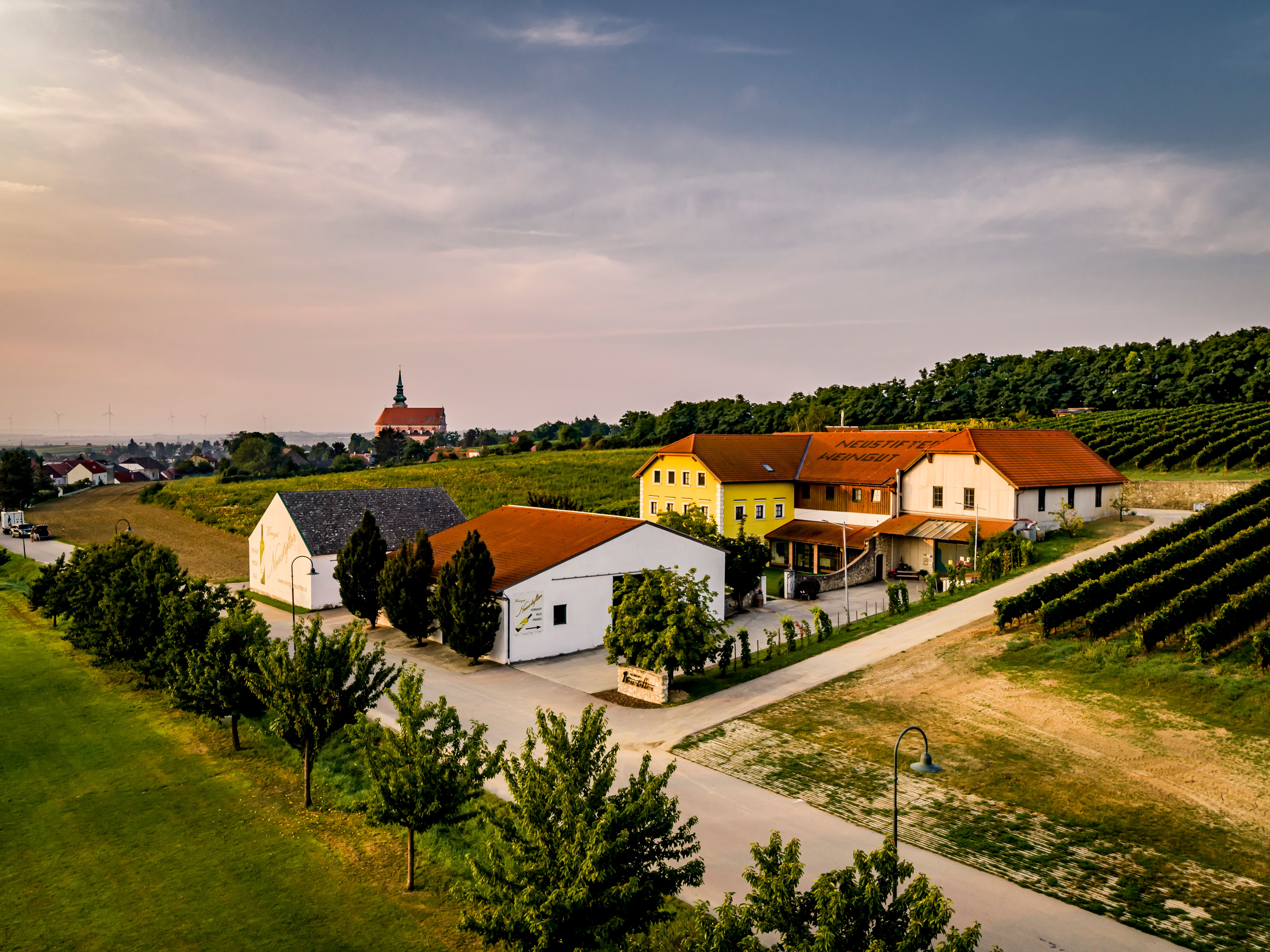Aerial view of a winery with buildings and vineyards at sunset.