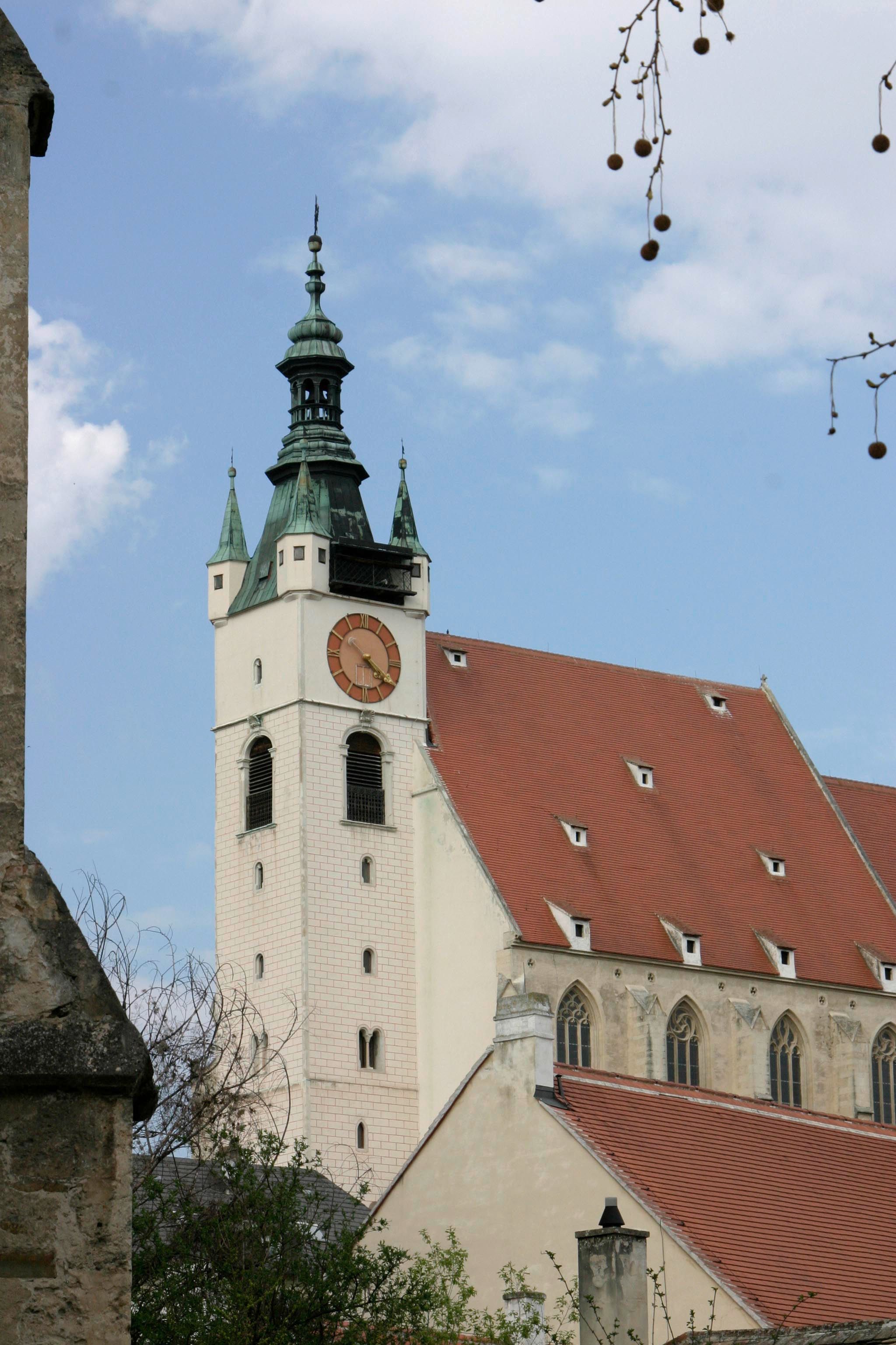 Piarist church with tower and clock against a blue sky.