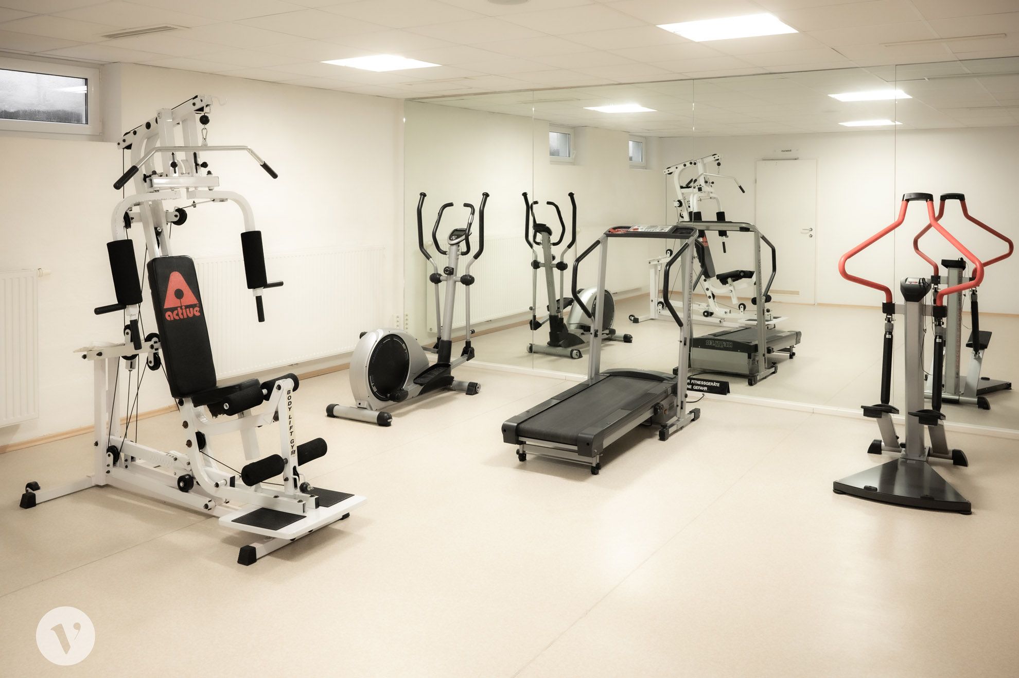 A fitness room with various training equipment such as a treadmill, exercise bike and weight station in front of a large mirror.
