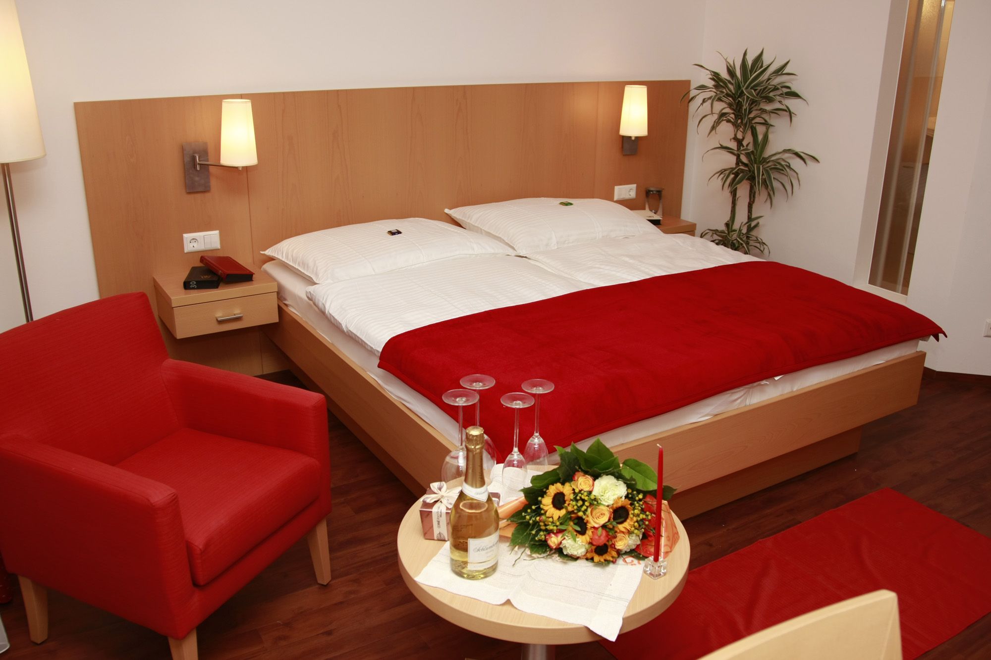 A cozy double room with a red armchair, bouquet of flowers and champagne on a table.