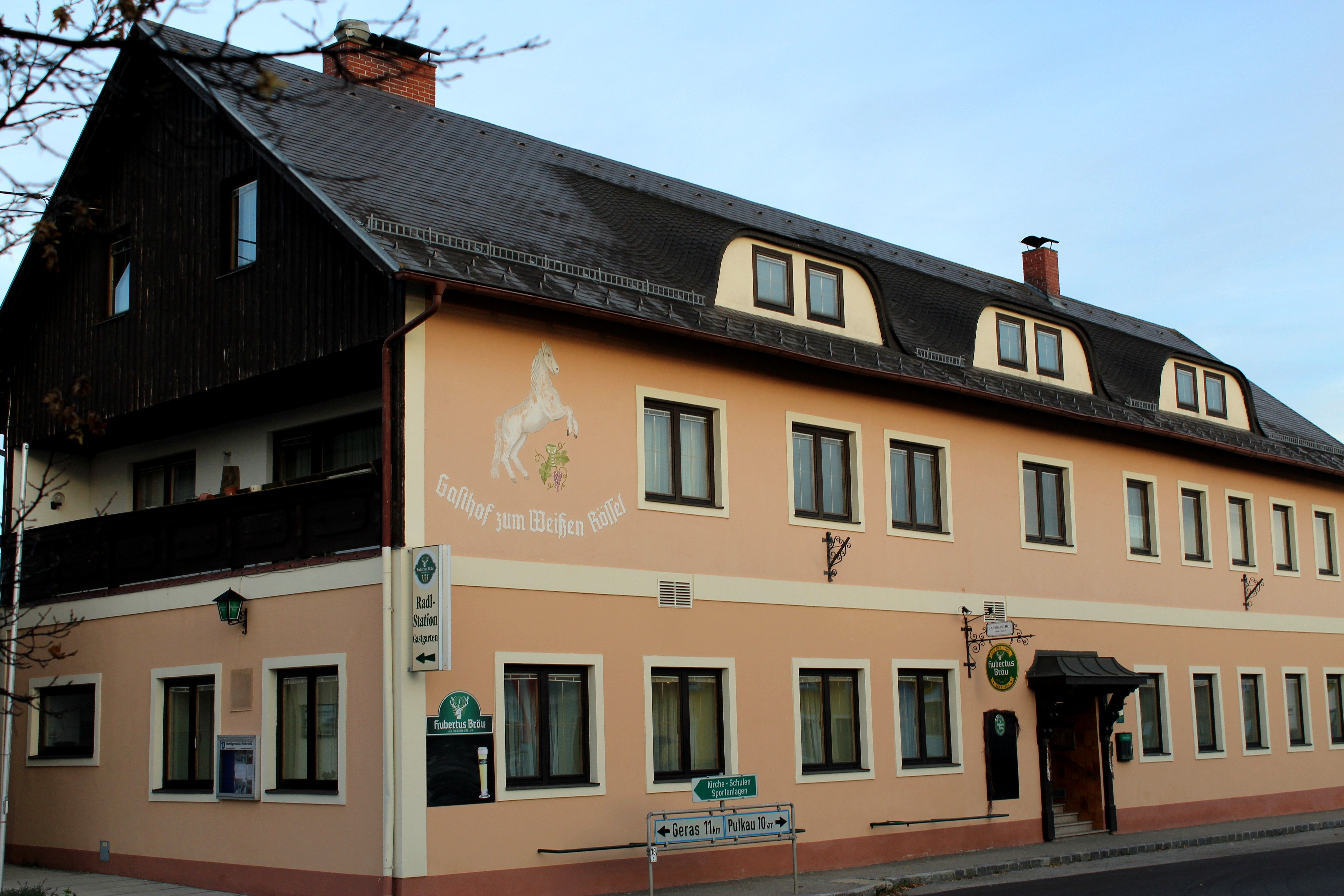 Exterior view of the inn 'Zum weißen Rössel' with beige façade and horse painting.