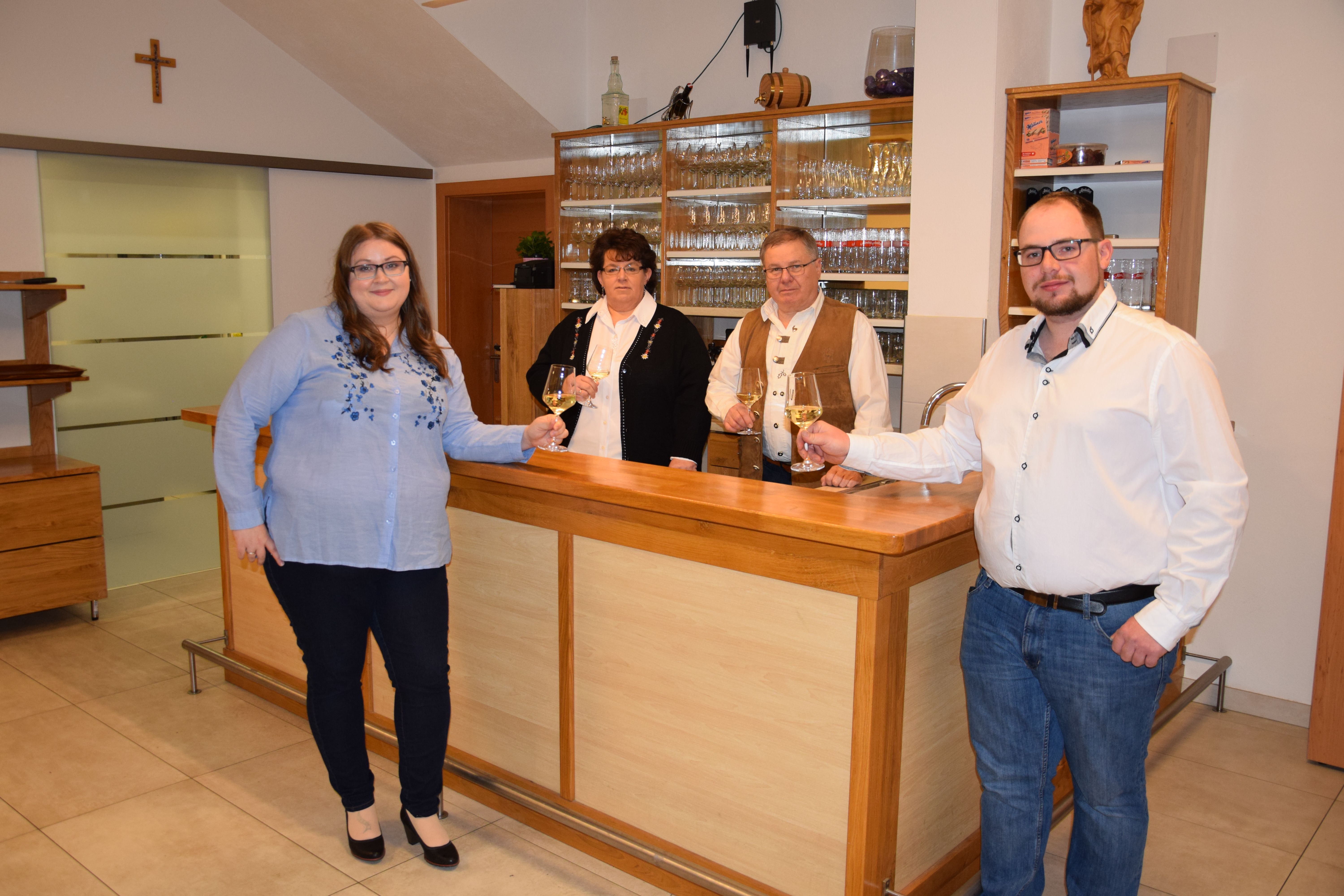Four people are standing at a bar holding glasses of wine.