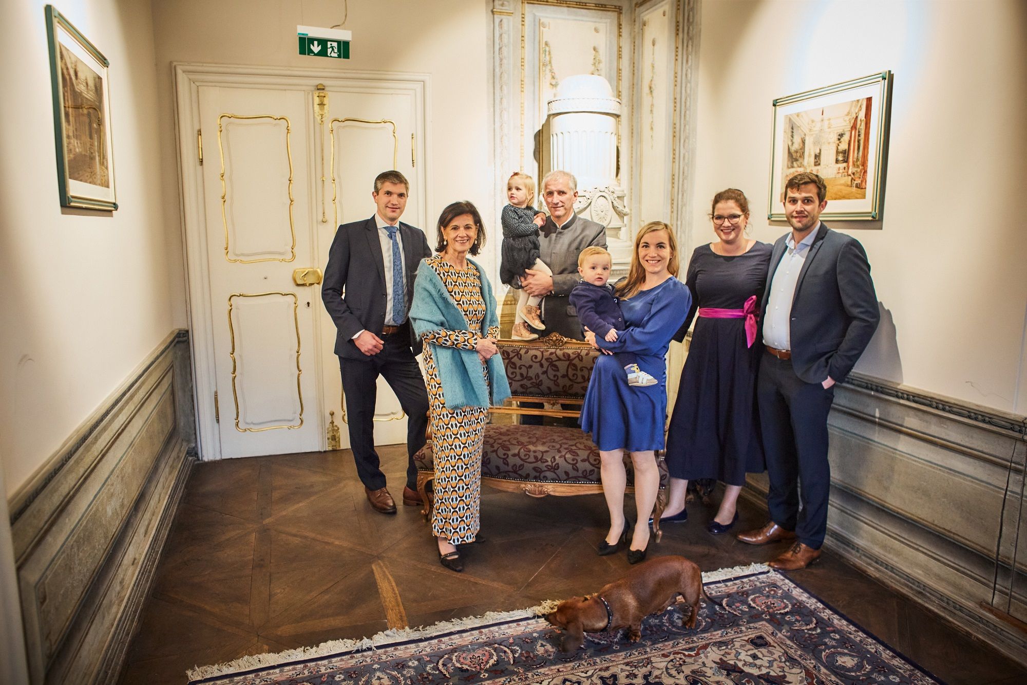 A group of people pose in an elegant room with a dog in the foreground.