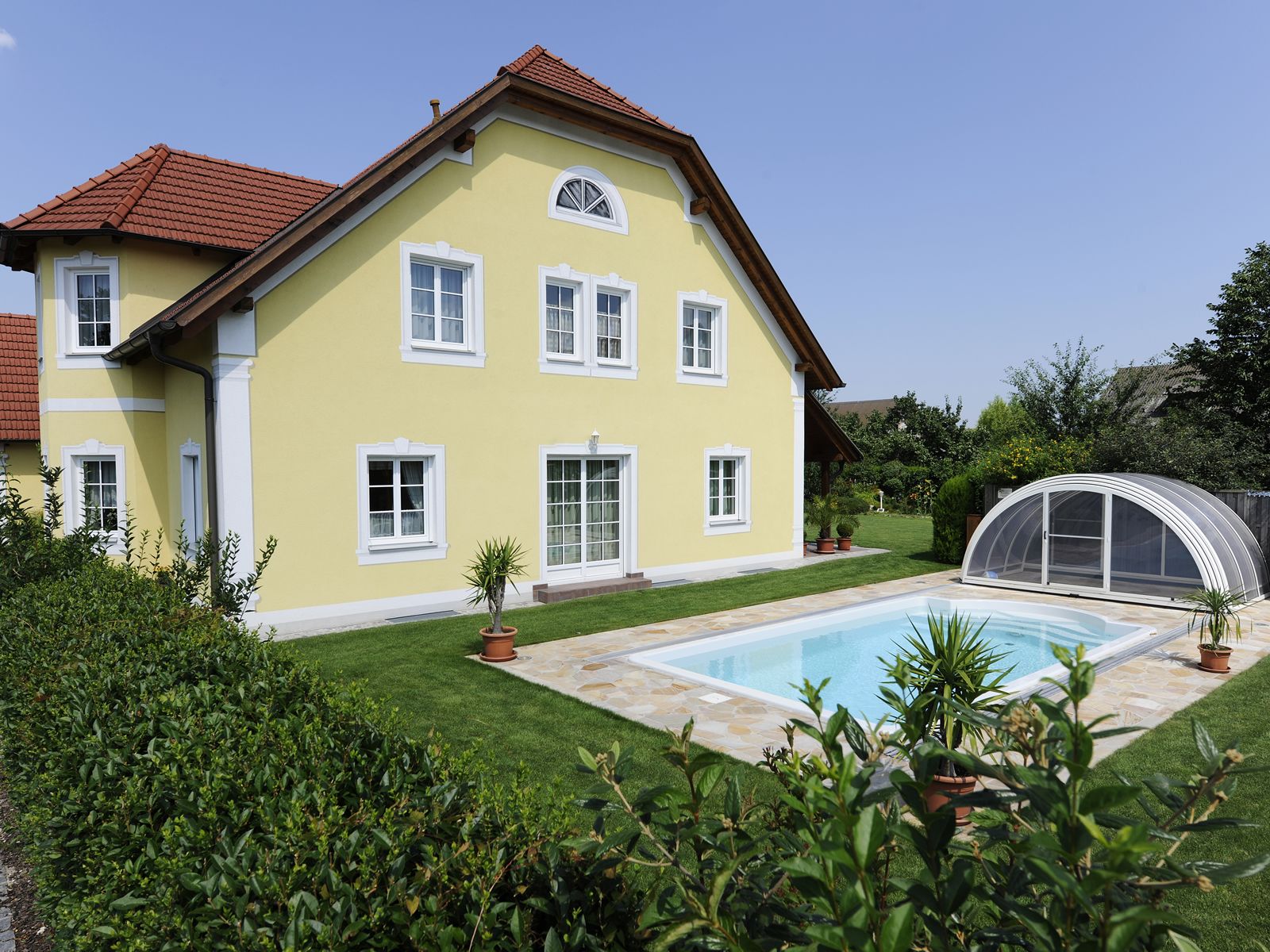 Yellow guest house with red roof and pool in the garden.