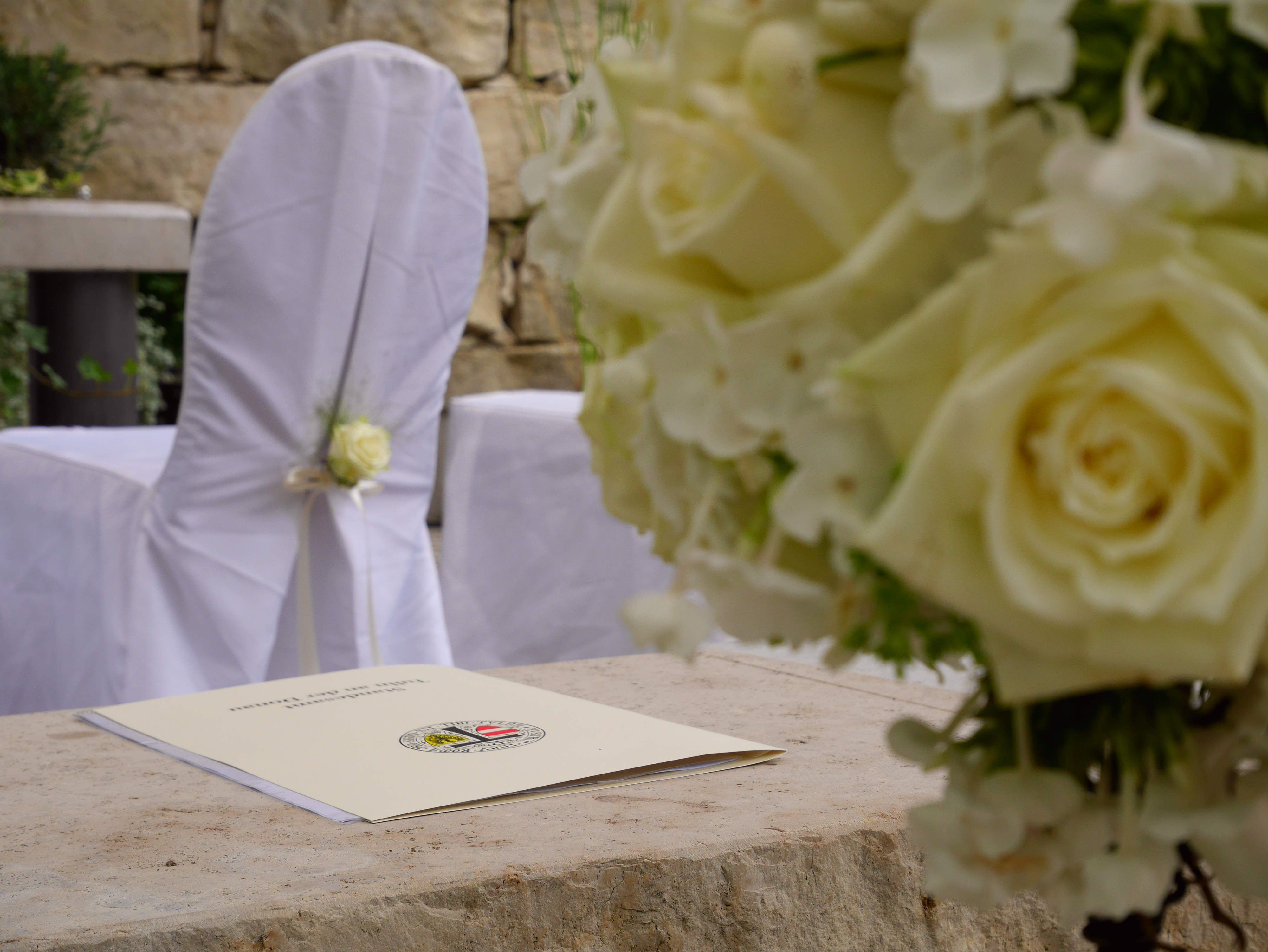 Close-up of a wedding decoration with white roses and a document on a table.